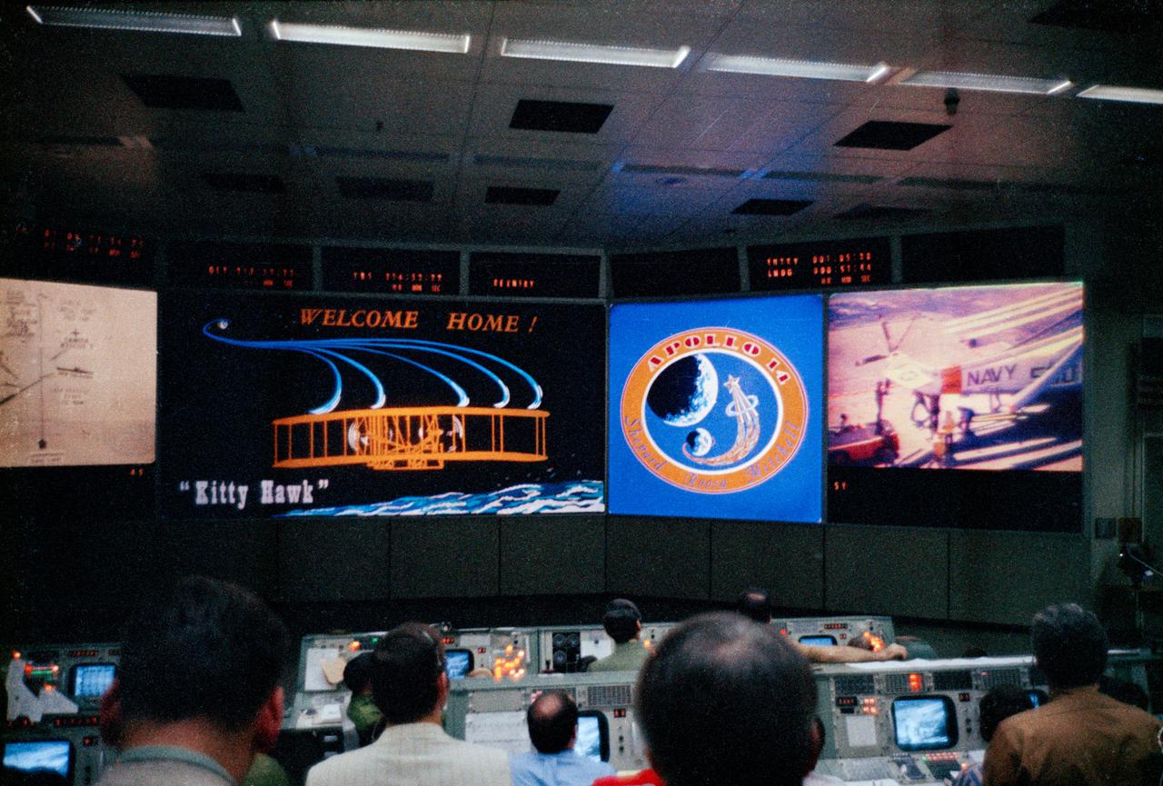 S71-18400 (9 Feb. 1971) --- Flight controllers in the Mission Operations Control Room (MOCR) of the Mission Control Center (MCC) view a colorful display which signals the successful splashdown and recovery of the crew of the Apollo 14 lunar landing mission. The MOCR's large screen at right shows a television shot aboard the USS New Orleans, Apollo 14 prime recovery ship.