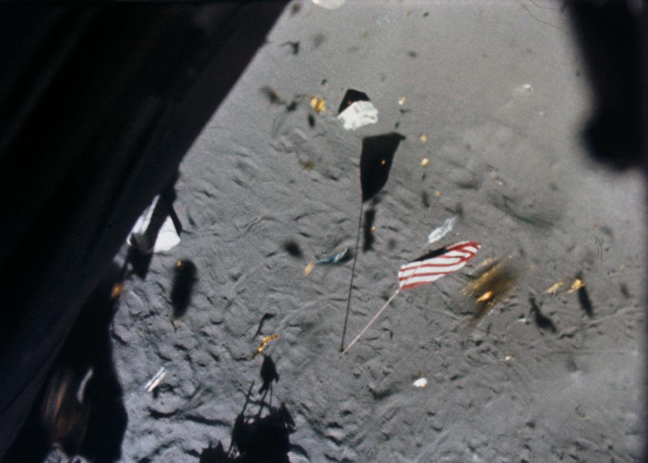 S71-19500 (6 Feb. 1971) --- The Apollo 14 Lunar Module (LM) ascent stage lifts off the lunar surface and the powerful LM engine causes a brief force of wind which scatters gold-colored foil, covering the LM, and disturbs the U.S. flag. This picture was taken from film exposed by the 16mm data acquisition camera - which was mounted inside the LM.