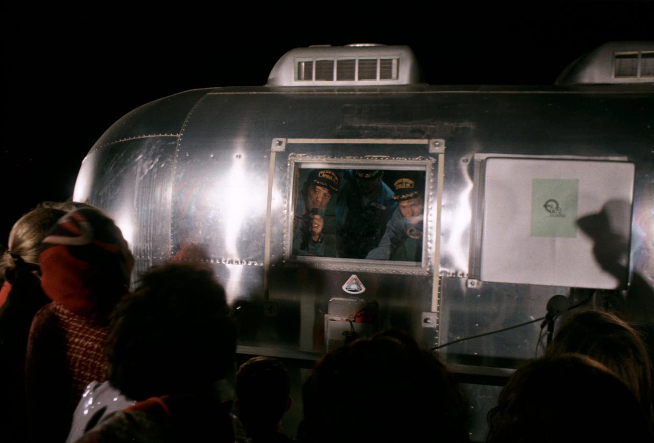 S71-19508 (12 Feb. 1971) --- Separated by aluminum and glass of their Mobile Quarantine Facility (MQF), the Apollo 14 crew members visit with their families and friends upon arriving at Ellington Air Force Base in the early morning hours of Feb. 12, 1971. Looking through the MQF window are astronauts Alan B. Shepard Jr. (left), commander; Stuart A. Roosa (right), command module pilot; and Edgar D. Mitchell, lunar module pilot. The crew men were brought to Houston aboard a C-141 transport plane from Pago Pago, American Samoa. The USS New Orleans had transported the crew to American Samoa from the recovery site in the South Pacific.