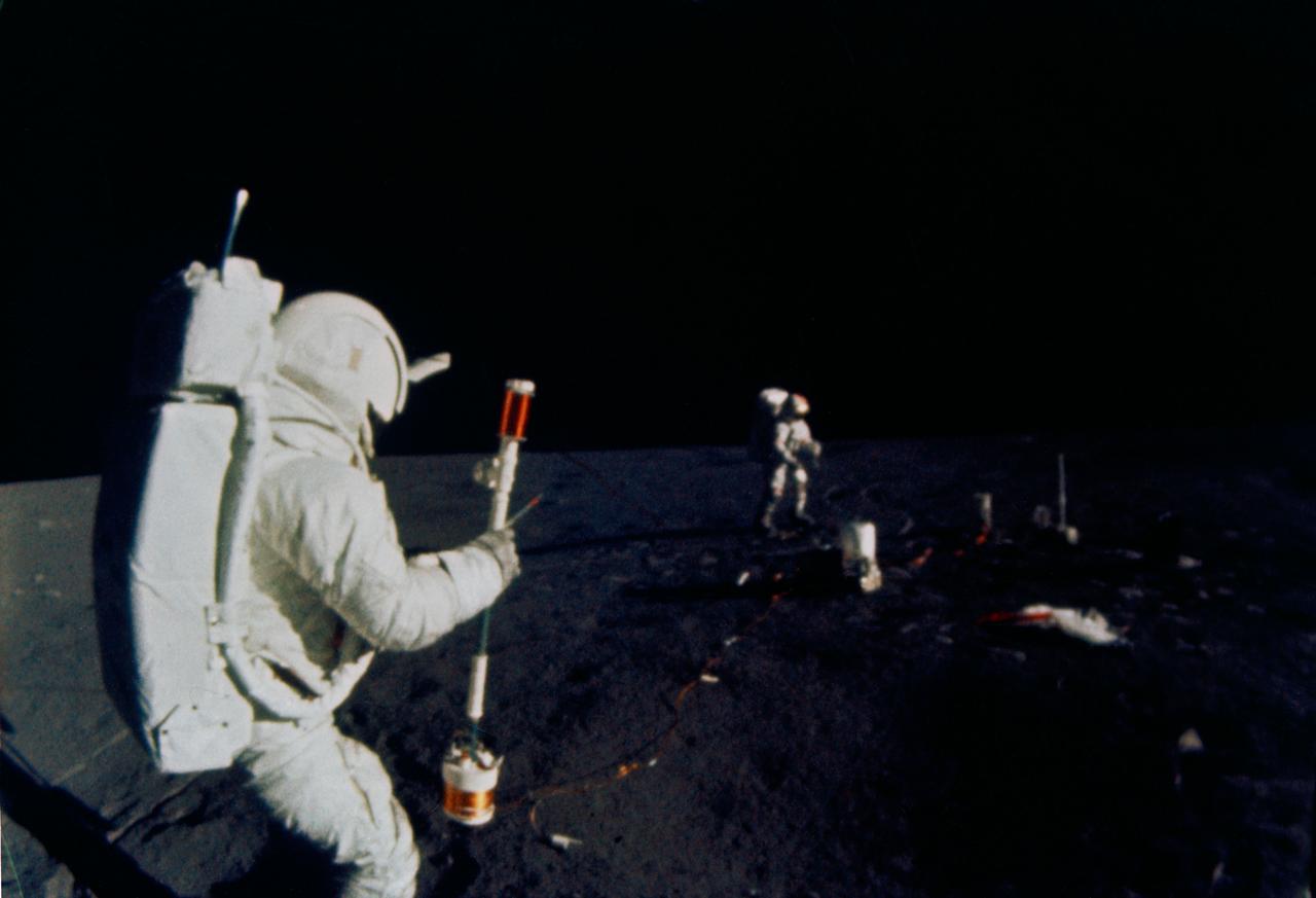 S71-19509 (5 Feb. 1971) --- Astronaut Edgar D. Mitchell, lunar module pilot, operates the Active Seismic Experiment's (ASE) thumper during the first Apollo 14 extravehicular activity (EVA) on the moon. Astronaut Alan B. Shepard Jr., commander, walks near deployed components of the Apollo Lunar Surface Experiments Package (ALSEP) in the background. This photograph was taken by an automatic 16mm camera mounted on the Apollo lunar hand tool carrier aboard the Modularized Equipment Transporter (MET). While astronauts Shepard and Mitchell descended in the LM to explore the moon, astronaut Stuart A. Roosa, command module pilot, remained with the Command and Service Modules (CSM) in lunar orbit.