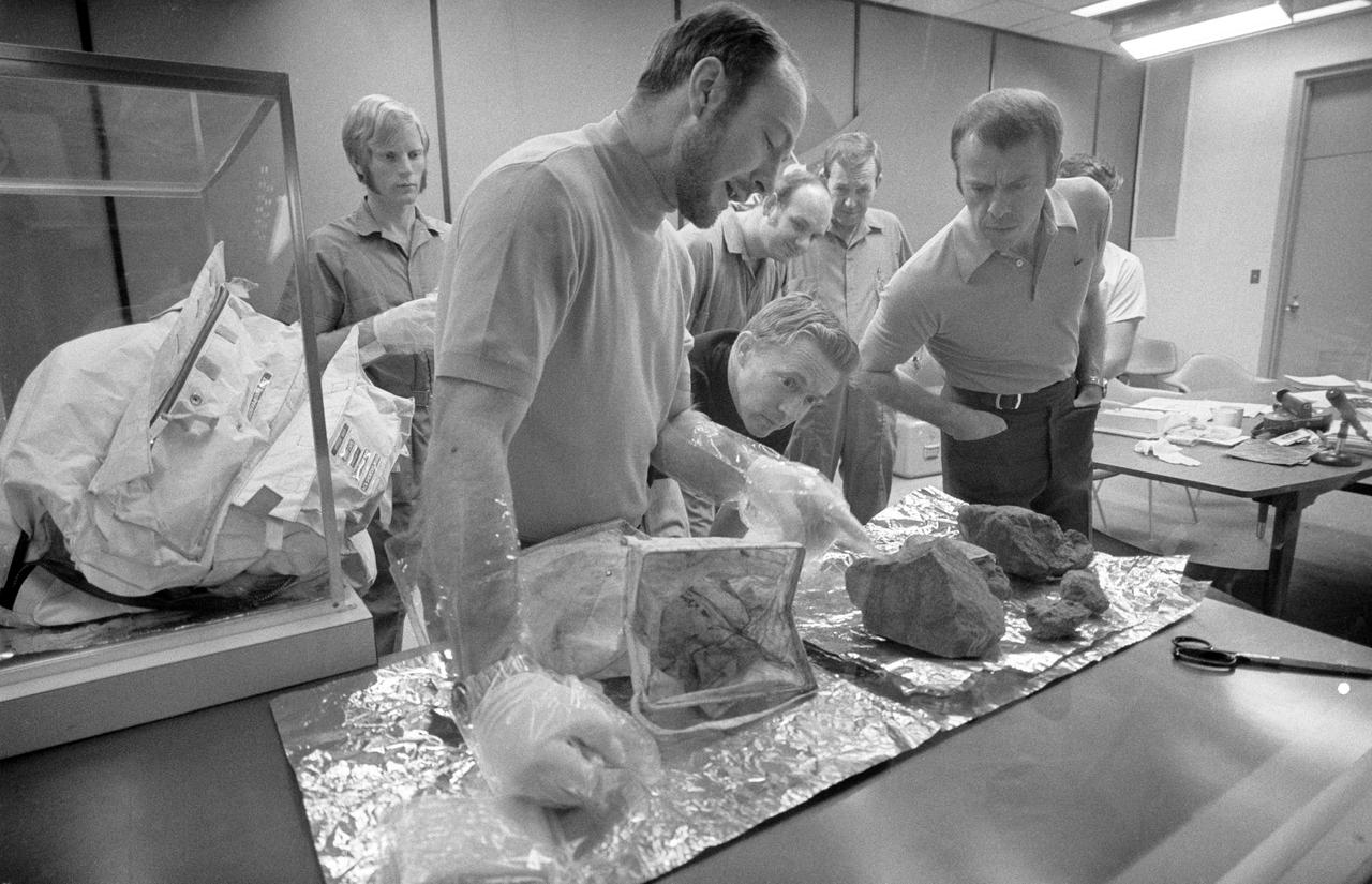 S71-20373 (19 Feb. 1971) --- The Apollo 14 crew men show off some of the largest of the lunar rocks which they brought back from the moon during a through-the-glass meeting with news men in the Crew Reception Area of the Lunar Receiving Laboratory (LRL) at the Manned Spacecraft Center (MSC). Astronaut Alan B. Shepard Jr. (right), mission commander, leans over to view a large basketball-size rock which astronaut Edgar D. Mitchell, lunar module pilot, points out. Astronaut Stuart A. Roosa, command module pilot, who circled the moon in the Command and Service Modules (CSM) while his two fellow crewmembers explored the moon, looks on (near the center of the photograph). Four of the 14 men quarantined with the Apollo 14 crew look on in the background.