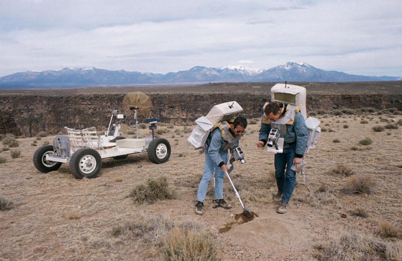 S71-23772 (11-12 March 1971) --- Two members of the prime crew of the Apollo 15 lunar landing mission collect soil samples during a simulation of lunar surface extravehicular activity in the Taos, New Mexico area. Astronaut James B. Irwin, lunar module pilot, is using a scoop. Astronaut David R. Scoot (right), commander, is holding a sample bag. On the left is a Lunar Roving Vehicle trainer.
