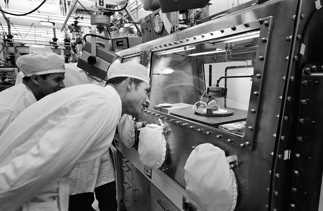S71-43477 (12 Aug. 1971) --- Astronaut David R. Scott, right, commander of the Apollo 15 mission, gets a close look at the sample referred to as "Genesis rock" in the Non-Sterile Nitrogen Processing Line (NNPL) in the Lunar Receiving Laboratory (LRL) at the Manned Spacecraft Center (MSC). Scientist-astronaut Joseph P. Allen IV, left, an Apollo 15 spacecraft communicator, looks on with interest. The white-colored rock has been given the permanent identification of 15415.