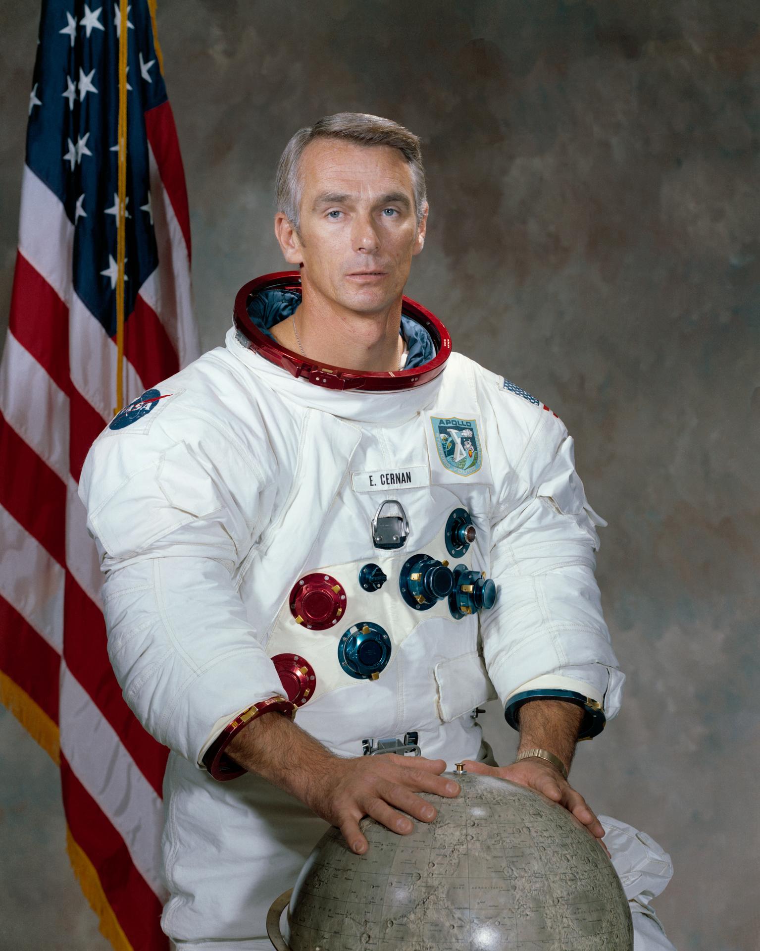 Official astronaut portrait of Eugene A, Cernan for the Apollo 10 mission. Hi is wearing his space suit, with his hands on a globe of the Moon. The American flag appears behind him.