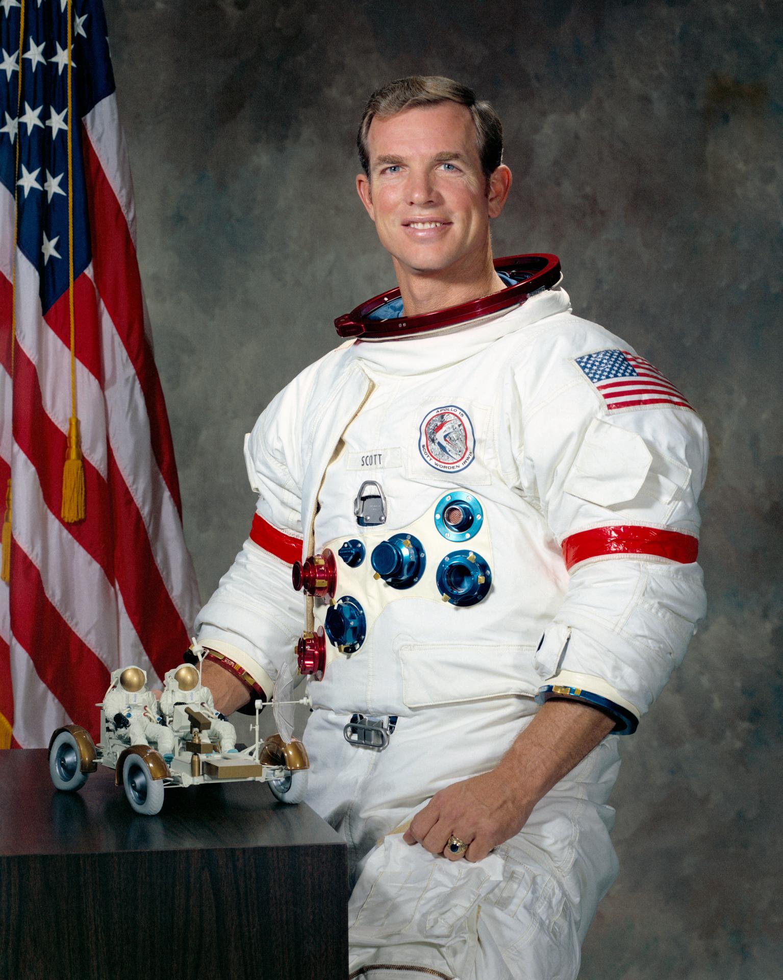 Portrait of astronaut David R. Scott in white spacesuit in front of US flag