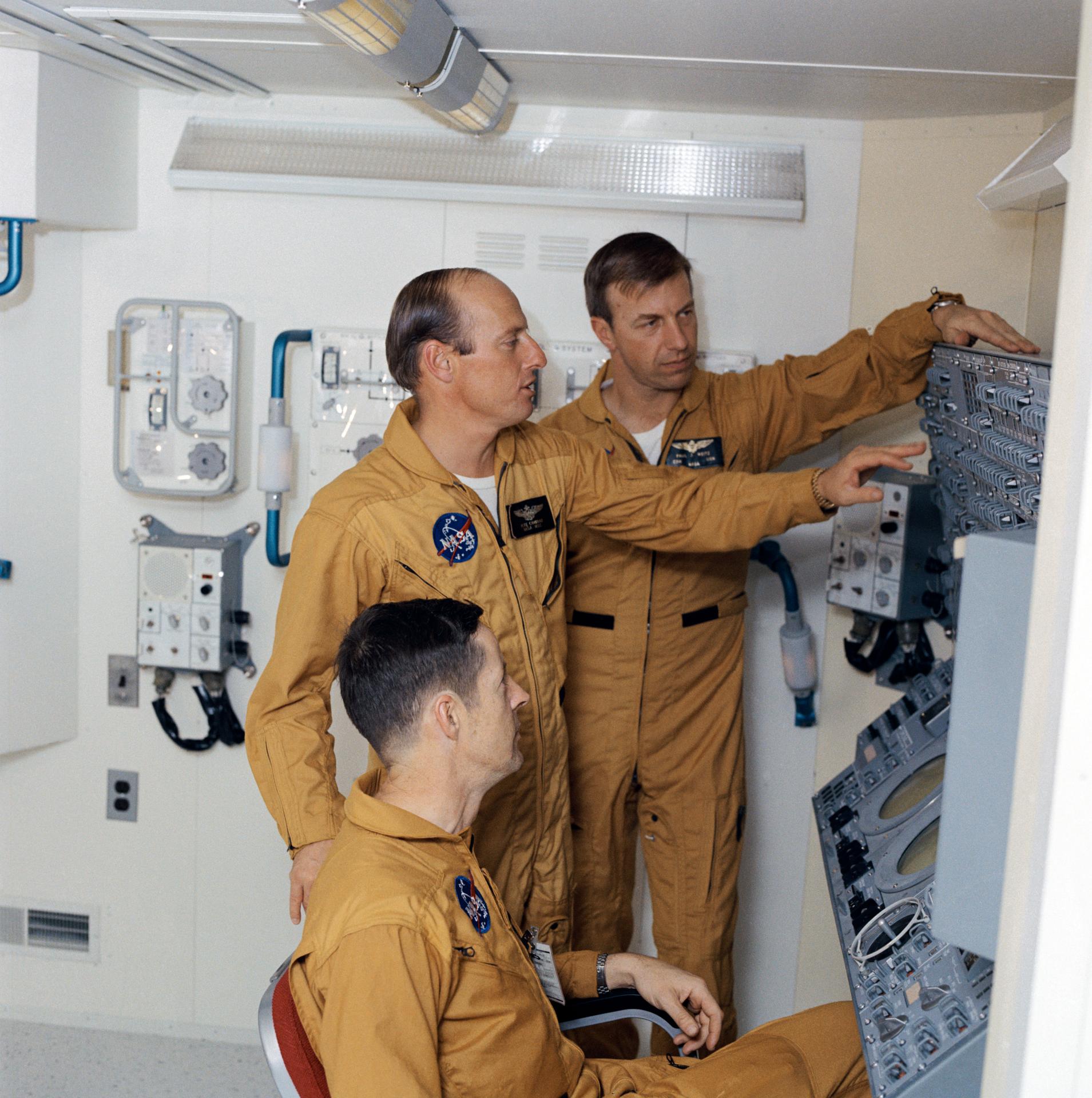 The Skylab 2 crew work at a training version of a Skylab control panel
