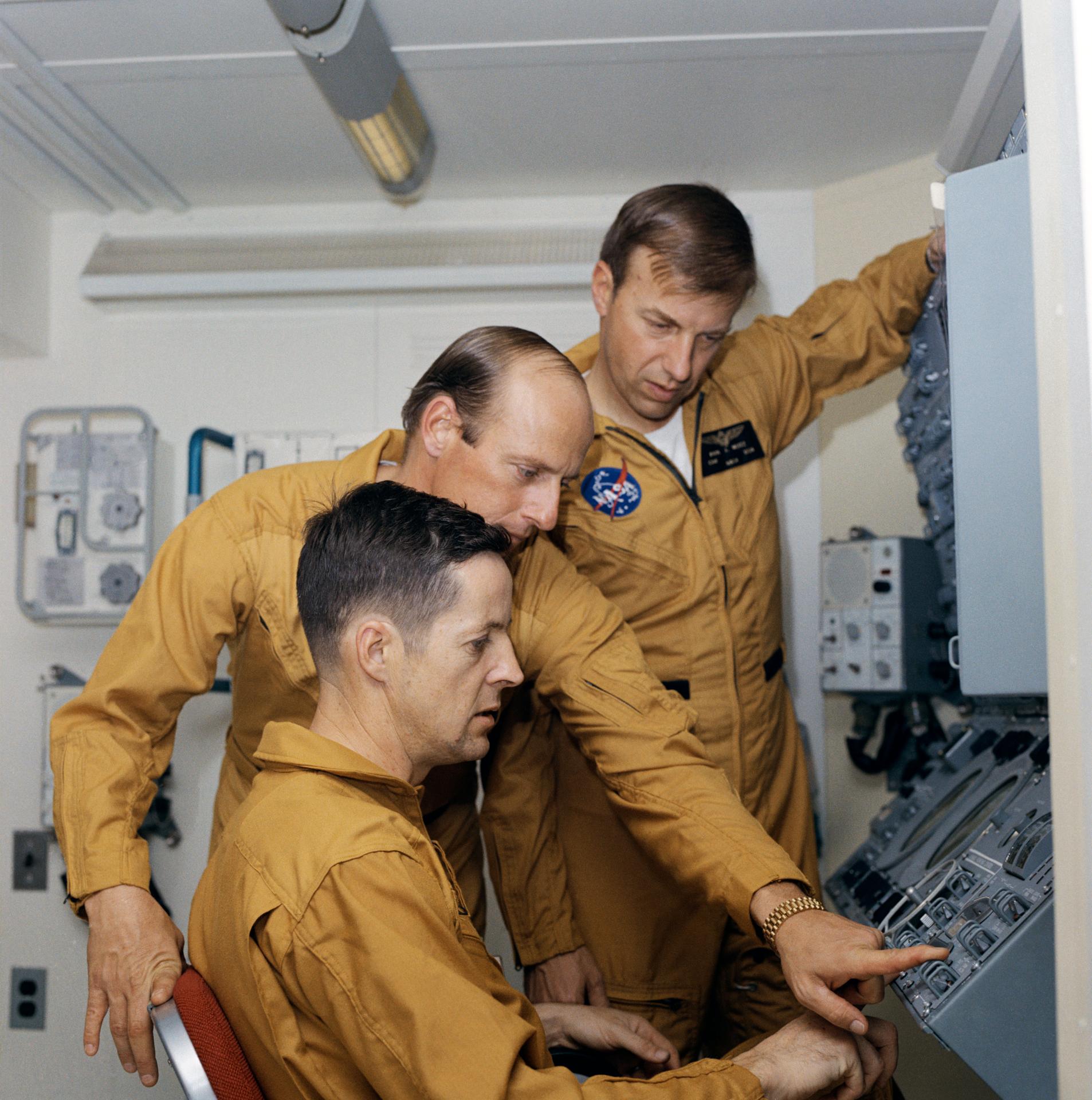 Joe Kerwin, Pete Conrad, and Paul Weitz wear tan flight suits while at the control panel for the Apollo Telescope Mount in the Training Facility in Houston Texas.