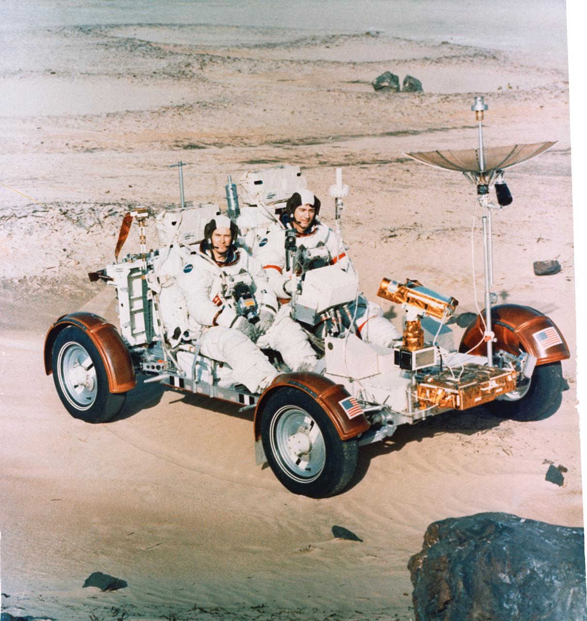 S72-30695 (22 Dec. 1971) --- Astronauts John W. Young, right, Apollo 16 commander, and Charles M. Duke Jr., lunar module pilot, maneuver a training version of the Lunar Roving Vehicle (LRV) about a field at Kennedy Space Center (KSC) simulated to represent the lunar surface. The LRV is planned to transport the two crew men around the Descartes area on the lunar surface while astronaut Thomas K. Mattingly II, command module pilot, orbits the moon in the Command and Service Modules (CSM).