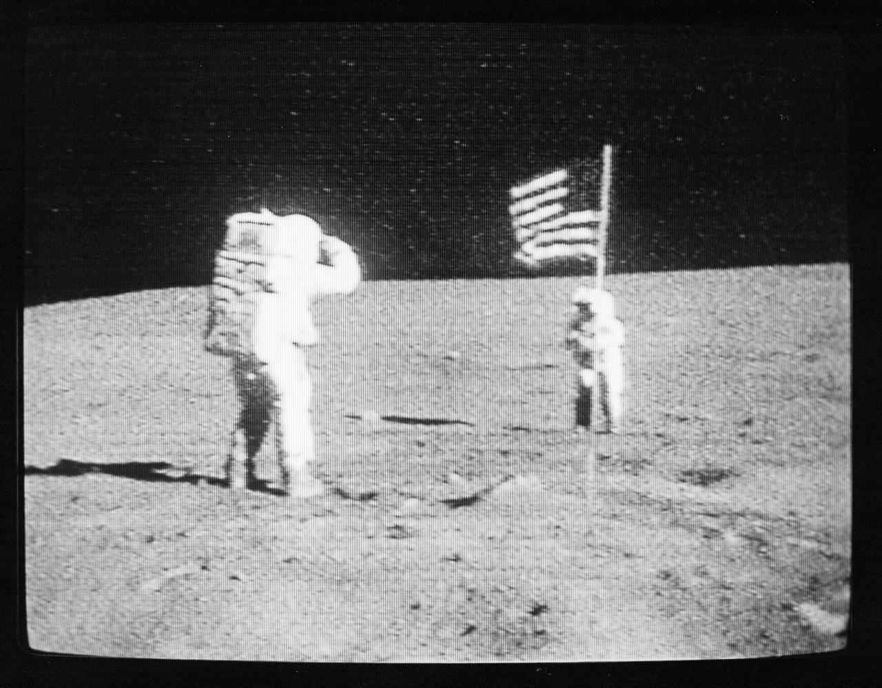 S72-35595 (21 April 1972) --- Astronaut Charles M. Duke Jr., lunar module pilot, salutes the United States flag during the first Apollo 16 extravehicular activity (EVA) on the moon, as seen in this black & white reproduction taken from a color television transmission made by the color TV camera mounted on the Lunar Roving Vehicle (LRV). Astronaut John W. Young, commander of the Apollo 16 lunar landing mission, stands beside the flag. While astronauts Young and Duke descended in the Apollo 16 Lunar Module (LM) "Orion" to explore the Descartes highlands landing site on the moon, astronaut Thomas K. Mattingly II, command module pilot, remained with the Command and Service Modules (CSM) "Casper" in lunar orbit.