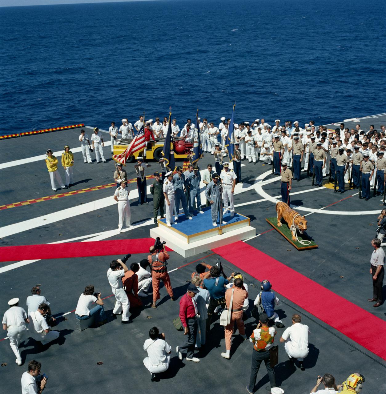 S72-36262 (27 April 1972) --- A high-angle view of the Apollo 16 welcoming aboard ceremonies on the deck of the prime recovery ship, USS Ticonderoga. It was soon after the splashdown of the Apollo 16 Command Module (CM) in the central Pacific Ocean approximately 215 miles southeast of Christmas Island. Astronaut John W. Young, commander, is standing at the microphone. Standing behind Young are astronaut Charles M. Duke Jr. (Left), lunar module pilot; and astronaut Thomas K. Mattingly II, command module pilot. The splashdown occurred at 290:37:06 ground elapsed time, 1:45:06 p.m. (CST), Thursday, April 27, 1972. The coordinates were 00:43.2 degrees south latitude and 156:11.4 degrees west longitude. The three crew members were picked up by helicopter and flown to the deck of the USS Ticonderoga.