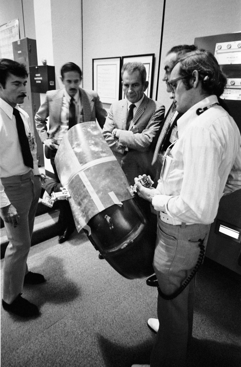 S72-55170 (11 Dec. 1972) --- These five men in the Mission Control Center ponder the solution to the problem of the damage to the right rear fender of the Apollo 17 Lunar Roving Vehicle at the Taurus-Littrow landing site. During the first lunar surface extravehicular activity a hammer got underneath the fender and a part of it was knocked off. Astronauts Eugene A. Cernan and Harrison H. Schmitt were reporting a problem with lunar dust because of the damaged fender. They sought some way to repair the broken fender. Clockwise are astronauts John W. Young and Charles M. Duke Jr., two Apollo 17 CAPCOM; Donald K. Slayton, director of flight crew operations at MSC; Dr. Roco A. Petrone, Apollo program director, Office of Manned Space Flight, NASA HQ; and Ronald V. Blevins, an EVA-1 flight controller with General Electric. They are looking over a makeshift repair arrangement which uses lunar maps and clamps from the optical alignment telescope lamp, a repair suggestion made by astronaut Young. The suggestion was relayed to Cernan and Schmitt and the repair made at the beginning of EVA-2. The problem was solved satisfactorily.