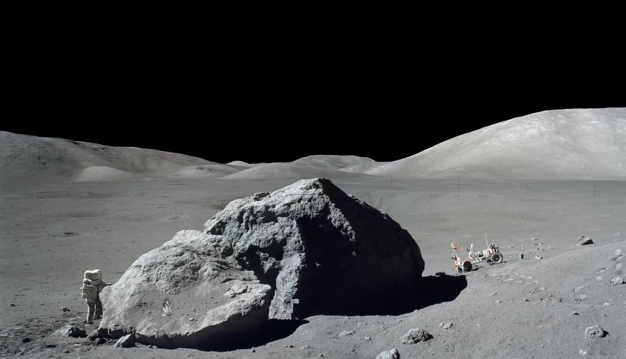 S73-22871 (13 Dec. 1972) --- Scientist-astronaut Harrison H. Schmitt is photographed standing next to a huge, split lunar boulder during the third Apollo 17 extravehicular activity (EVA) at the Taurus-Littrow landing site. The Lunar Roving Vehicle (LRV), which transported Schmitt and Eugene A. Cernan to this extravehicular station from their Lunar Module (LM), is seen in the background. The mosaic is made from two frames from Apollo 17 Hasselblad magazine 140. The two frames were photographed by Cernan.