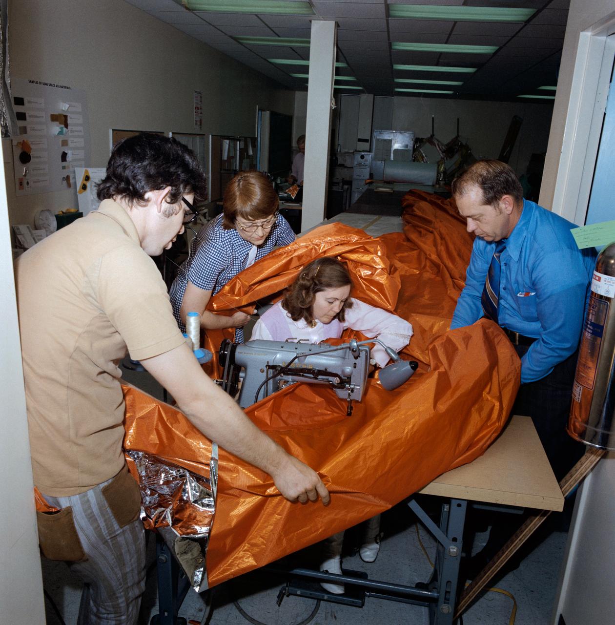S73-26047 (18 May 1973) --- A sail-like sunshade for possible use as a sunscreen for the Skylab orbital workshop (OWS) is shown being fabricated in the GE Building across the street from the Johnson Space Center. Three persons assist the seamstress feed the material through the sewing machine. The three-layered shade will be composed of a top layer of aluminum Mylar, a middle layer of laminated nylon rip stop, and a bottom layer of thin nylon. Working on the sunshade, from left to right, are Dale Gentry, Elizabeth Gauldin, Alyene Baker and James H. Barnett Jr. Mrs. Baker, a GE employee, operates the double-needle sewing machine. Barnett is head of the Crew Equipment Development Section of JSC's Crew Systems Division. Mrs. Gauldin is also with the Crew Systems Division. Gentry works for GE. The work shown here is part of the crash program underway to prepare a protection device for Skylab to replace the original shield which was lost when the unmanned Skylab 1 launch took place on May 14, 1973. The improvised solar shield selected to be used will be carried to Earth orbit by the Skylab 2 crew, who will deploy it to shade part of the OWS from the hot rays of the sun. Loss of the original shield, as expected, has caused an overheating problem on the OWS. Photo credit: NASA