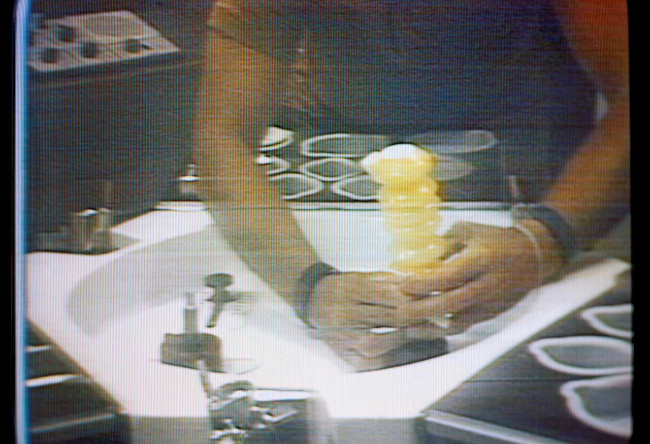S73-27078 (30 May 1973) --- An accordian-style beverage dispenser filled with orange juice is held by astronaut Charles Conrad Jr., Skylab 2 commander, in this close-up view which is a reproduction taken from a color television transmission made by a TV camera aboard the Skylab 1 & 2 space station cluster in Earth orbit. Conrad (head and face not in view) is seated at the wardroom table in the crew quarters of the Orbital Workshop. The dispenser contained beverage crystals, and Conrad has just added the prescribed amount of water to make the orange drink. Photo credit: NASA