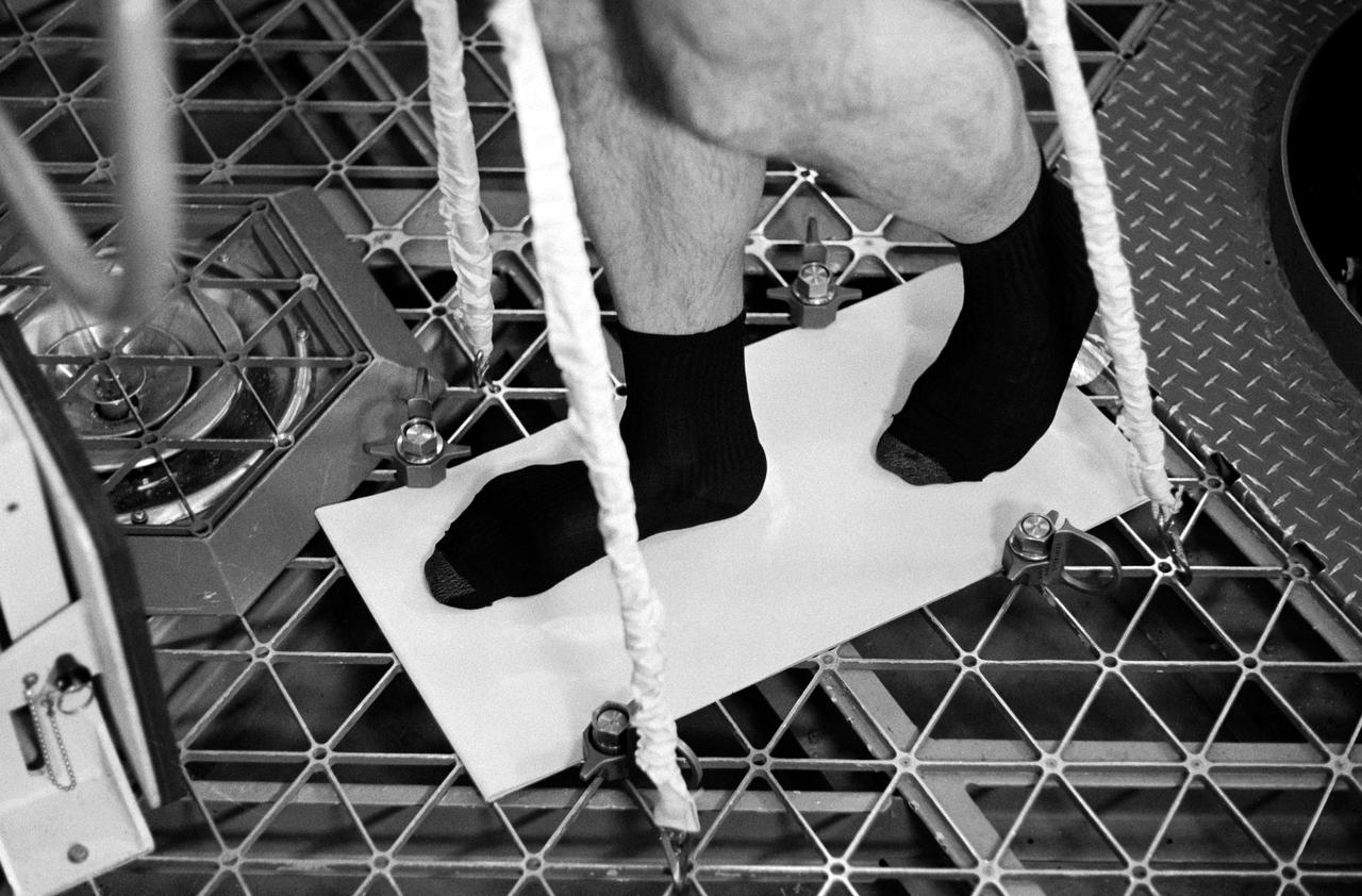 S73-33858 (November 1973) --- A close-up view of the feet of scientist-astronaut William E. Thornton as he demonstrates the use of a treadmill-like exercise device which was developed for maintaining the leg and back muscles of the Skylab 4 crewman. Thornton is in the Skylab Orbital Workshop simulator in Building 5 at the Johnson Space Center. The Skylab 2 and Skylab 3 astronauts had no exercise device onboard capable of adequately maintaining their leg and back muscles. The treadmill device consists of a Teflon-coated aluminum plate or sheet bolted to the floor of the Skylab Orbital Workshop. The crewmen will wear the bicycle ergometer harness while exercising. Bungee cords attached to the floor and to the harness will supply the downward pressure or force for the back and leg muscles. The astronaut's feet will slide over the Teflon-coated plate as he "marches in place." Photo credit: NASA