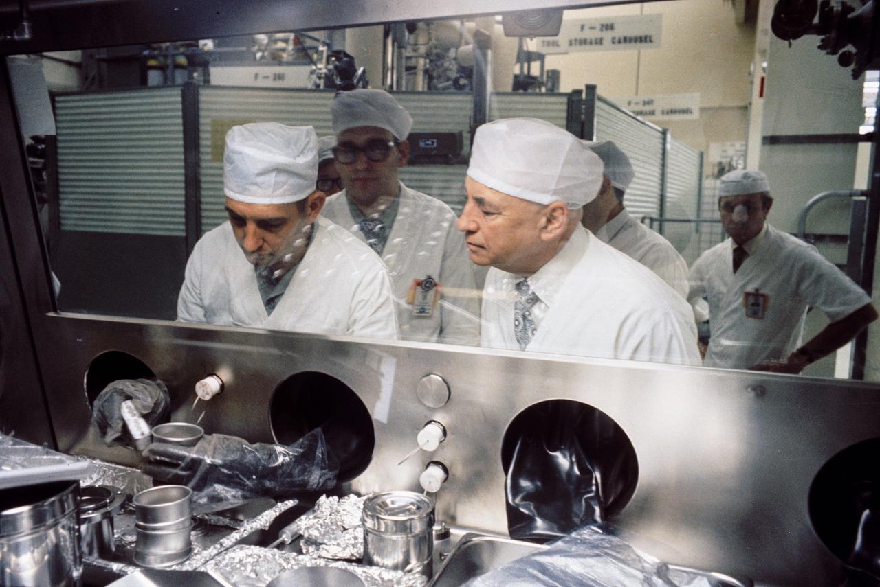 S73-34103 (1973) --- Wearing special germ-free clothing, Dr. Robert R. Gilruth, right, inspects lunar samples collected during the Apollo 17 mission, NASA's final Apollo flight.