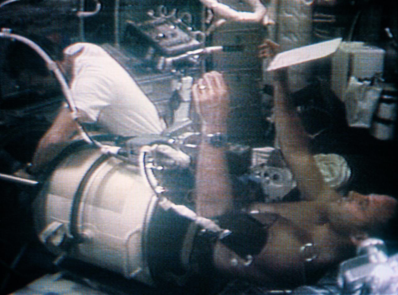 S73-34180 (7 Aug. 1973) --- A medium close-up view of astronaut Jack R. Lousma, Skylab 3 pilot, in the Lower Body Negative Pressure Device (LBNPD), as astronaut Alan L. Bean, commander, works around the leg band area. This portion of the LBNPD MO-92 experiment was televised on Aug. 7, 1973. The LBNPD experiment is to provide information concerning the time course of cardiovascular adaptation during flight, and to provide in-flight data for predicting the degree of orthostatic intolerence and impairment of physical capacity to be expected upon returning to Earth environment. The bicycle ergometer is in the background, partially visible behind Bean. Photo credit: NASA