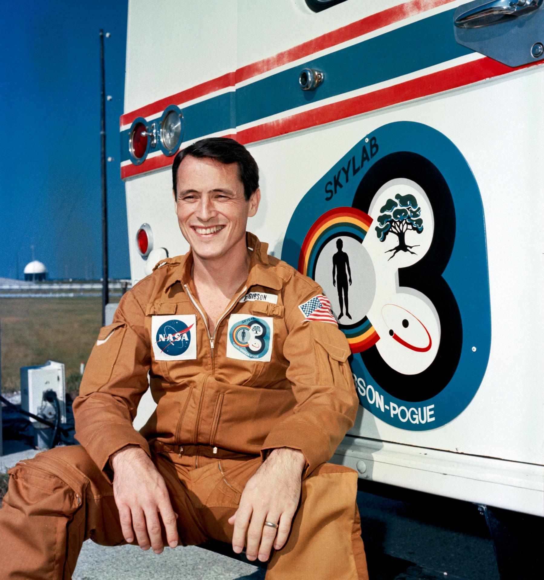 Astronaut Ed Gibson poses next to the Skylab 4 insignia on the transfer van.