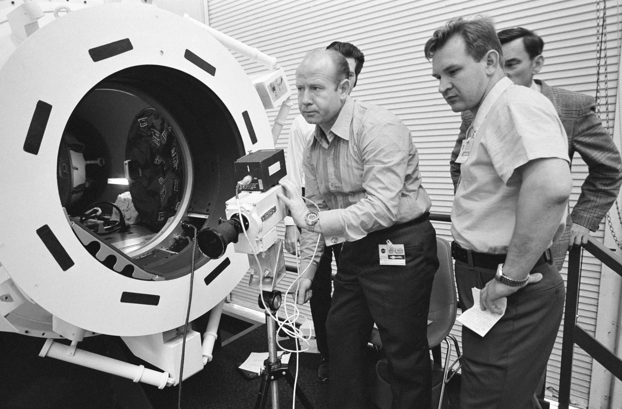 S74-20794 (23 April 1974) --- Cosmonaut Aleksey A. Leonov (center), commander of the Soviet crew of the joint U.S.-USSR Apollo-Soyuz Test Project mission, goes through familiarization training with a television camera during ASTP activity at the Johnson Space Center. Cosmonaut Valeriy N. Kubasov (right), engineer on Leonov?s crew, is looking on. An ASTP docking module mock-up is on the left. Interpreter K.S. Samofal is behind Kubasov. David Brooks, with JSC?s Crew Procedures Division, is in the left background. This phase of the ASTP communications training was conducted in JSC?s Building 35. The equipment being used in the picture is an early design of the Westinghouse TV camera.