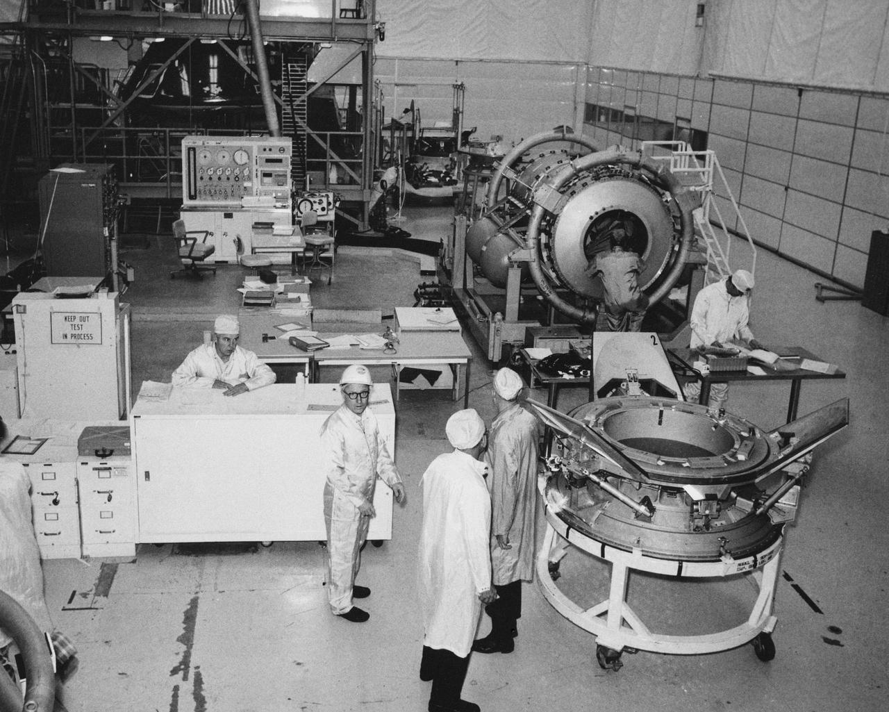 S74-28295 (September 1974) --- American-built hardware for the joint U.S.-USSR Apollo-Soyuz Test Project mission undergoes pre-delivery preparations in the giant clean room at Rockwell International Corporation?s Space Division at Downey, California. The U.S. portion of the ASTP docking system is in the right foreground. In the right background is the cylindrical-shaped docking module, which is designed to link the Apollo and Soyuz spacecraft when they dock in Earth orbit next summer. In the left background is the Apollo Command Module which they will carry the three American astronauts into Earth orbit.  Photo credit: NASA