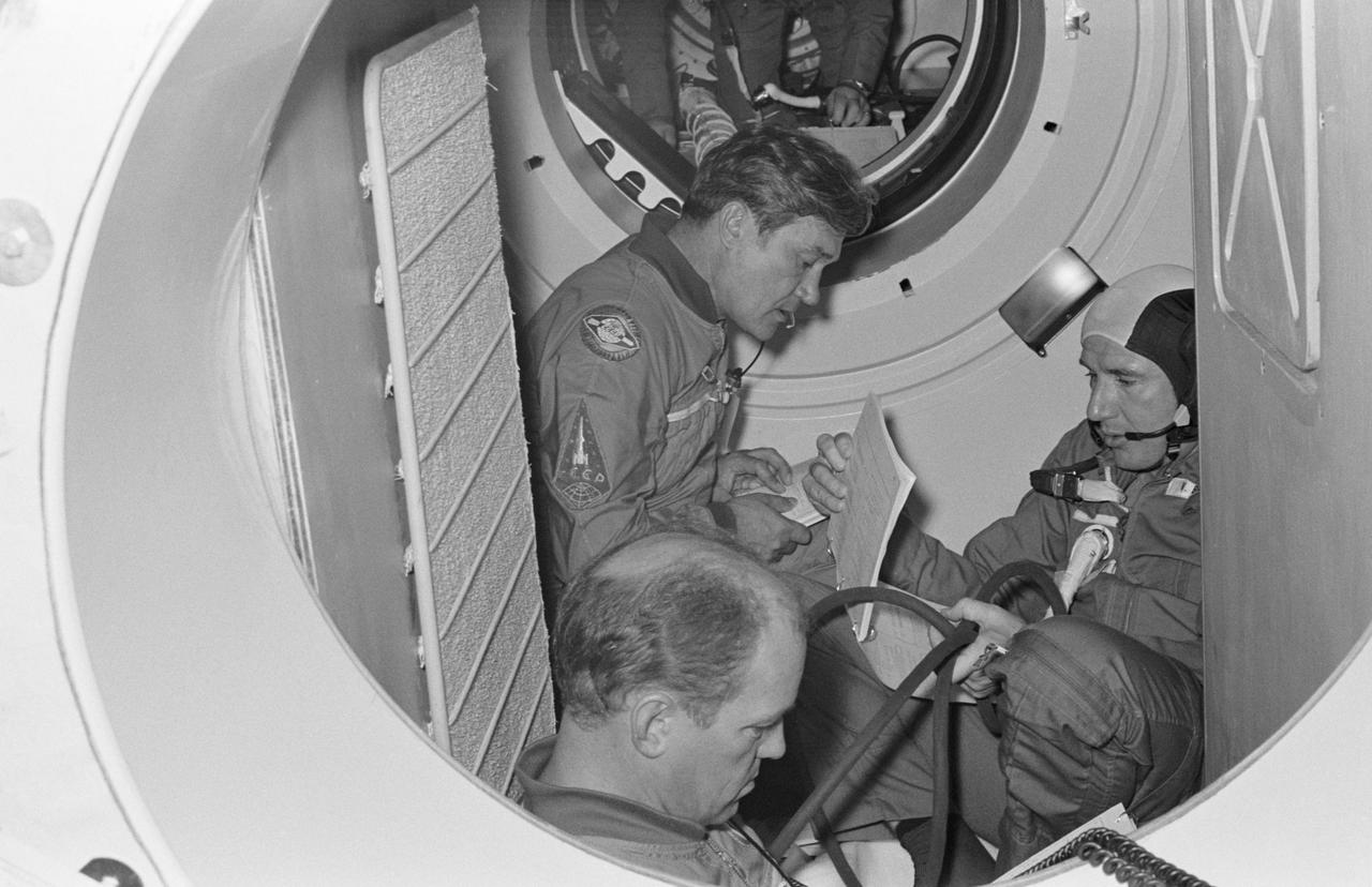 S74-28649 (16 Sept. 1974) --- Three crewmen of the Apollo-Soyuz Test Project are seated in a Soviet Soyuz spacecraft orbital module mock-up in Building 35 during ASTP simulation training at the Johnson Space Center. They are cosmonaut Anatoliy V. Filipchenko (left background), commander of the Soviet ASTP second (backup) crew; cosmonaut Nikolay N. Rukavishnikov (left foreground), engineer on the crew; and astronaut Vance D. Brand (right), command module pilot of the American ASTP prime crew. The hatch in the background leads to the Docking Module. During the exercise the American ASTP crew and the Soviet ASTP crew simulated docking the Apollo and Soyuz in Earth orbit and transferring to each other?s spacecraft. Here, Brand is visiting the Soyuz spacecraft. The crewmen are training in both the U.S. and the USSR for the joint mission scheduled for the summer of 1975.