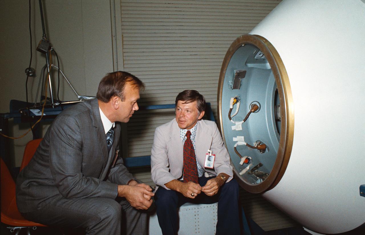 S74-32481 (November 1974) --- These two men are flight directors for the joint U.S.-USSR Apollo-Soyuz Test Project mission scheduled for July 1975. Cosmonaut Aleksey A. Yeliseyev (left) is the Soviet ASTP senior flight director; M.P. Frank is the American ASTP senior flight director. They are seated beside a Docking Module training mock-up in Building 35 at the Johnson Space Center. Cosmonaut Yeliseyev was head of a delegation of USSR flight controllers who were at JSC for two weeks of ASTP training.
