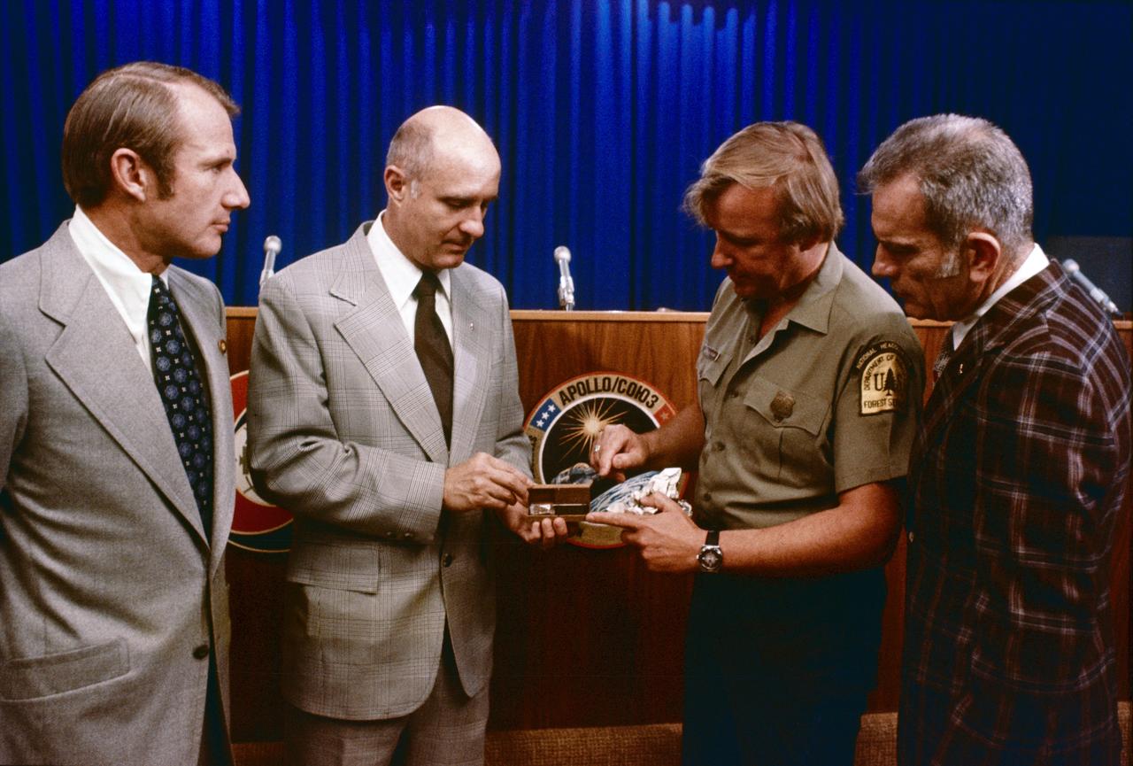 S75-27445 (6 June 1975) --- American ASTP crewmen Vance D. Brand (left), Thomas P. Stafford (second from left) and Donald K. Slayton (right) receive a special box of genetically superior white spruce seeds from Glenn A. Kovar (second from right), USDA Forest Service project coordinator. The seeds, enough to plant an acre of trees, will be presented to the Soviet ASTP crewmen during the U.S.-USSR Apollo-Soyuz Test Project docking-in-Earth-orbit mission in July 1975.  The seeds will produce faster-growing trees of exceptional height and shape. The trees will thrive in Moscow-like climate, and were developed by Forest Service?s Institute of Forest Genetics in Rhinelander, Wisconsin.  The seed container box was made from recycled fibers and stabilized walnut. These seeds are an outstanding example of the U.S. Forest Service research to help produce new improved forests for the world. The four men are standing in the Building 2 briefing room at NASA's Johnson Space Center.