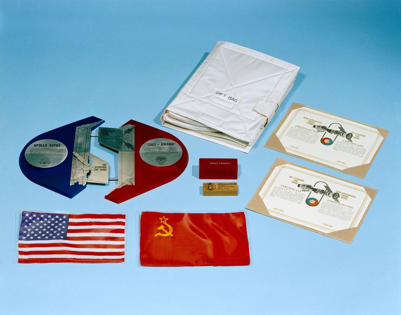 S75-27952 (July 1975) --- A close-up view of the special ?gift bag? in which several exchange/gift items will be carried aboard the Apollo Command Module during the joint U.S.-USSR Apollo-Soyuz Test Project mission. Some of these items are seen here alongside the bag. They are the sectionized ASTP Commemorative Plaque, ten 8x12 inch American flags, ten 8.07x16.14 inch (205mm x 410mm) Soviet Union flags, a special box of white spruce tree seeds, and the ASTP Certification to authorize the ASTP docking. The gifts will be presented and the exchange made while the Apollo and Soyuz spacecraft are docked in Earth orbit.
