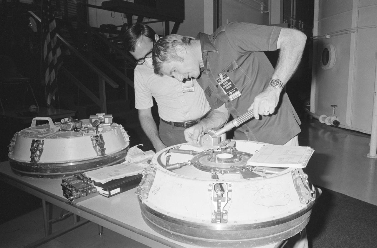 S75-28485 (12 July 1975) --- Astronaut Vance D. Brand, command module pilot of the American ASTP prime crew, practices operating a Docking Module hatch during Apollo-Soyuz Test Project preflight training at NASA's Johnson Space Center. The Docking Module is designed to link the Apollo and Soyuz spacecraft during their docking mission in Earth orbit. Gary L. Doerre of JSC?s Crew Training and Procedures Division is working with Brand. Doerre is wearing a face mask to help prevent possible exposure to Brand of disease prior to the ASTP launch.