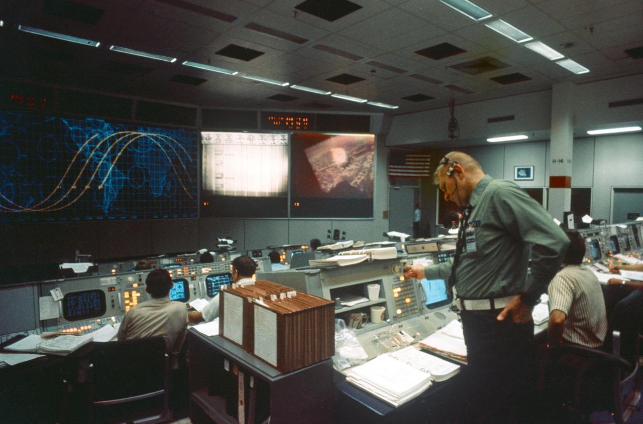 S75-28682 (17 July 1975) --- An overall view of the Mission Operations Control Room in the Mission Control Center during the joint U.S.-USSR Apollo-Soyuz Test Project docking mission in Earth orbit. The large television monitor shows a view of the Soyuz spacecraft as seen from the Apollo spacecraft during rendezvous and docking maneuvers. Eugene F. Kranz, JSC Deputy Director of Flight Operations, is standing in the foreground. M.P. Frank, the American senior ASTP flight director, is partially obscured on the right.