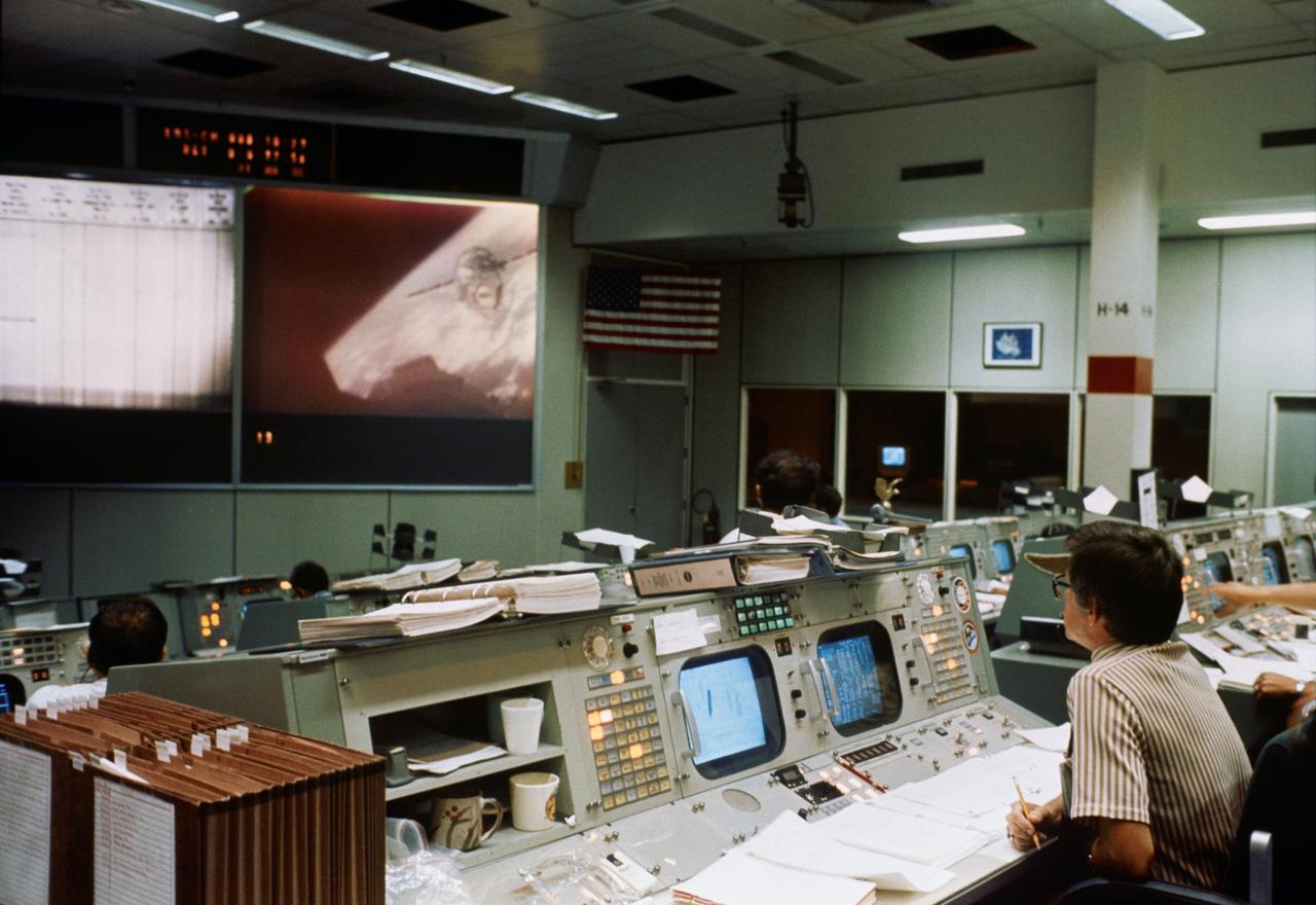 S75-28683 (17 July 1975) --- An overall view of the Mission Operations Control Room in the Mission Control Center during the joint U.S.-USSR Apollo-Soyuz Test Project docking mission in Earth orbit. M.P. Frank, the American senior ASTP flight director, is seated at his console in the right foreground. He is watching the large television monitor which shows a view of the Soyuz spacecraft as seen from the Apollo spacecraft during rendezvous and docking maneuvers.
