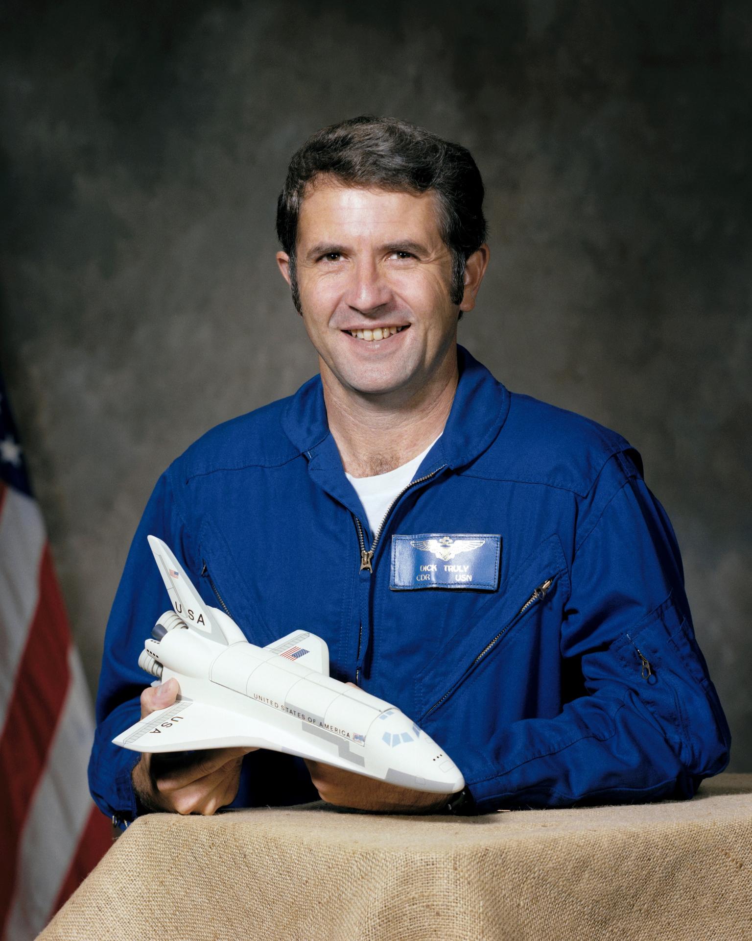 Portrait of astronaut Richard H. Truly taken in 1976. He holds a model of a space shuttle orbiter and is wearing a blue flight suit.