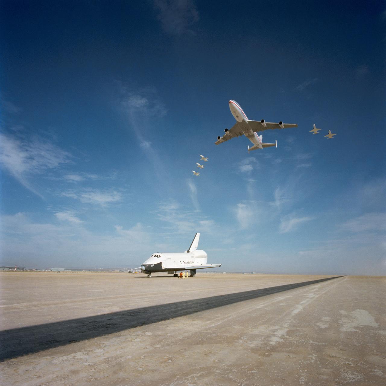 S77-28200 (13 Sept 1977) --- This impressive scene was photographed when the NASA 747 carrier aircraft and five T-38 aircraft flew over the shuttle Orbiter 101 "Enterprise" while it was parked on the runway at Edwards Air Force Base in Southern California.  The Orbiter 101 had just completed a five-minute, 28-second unpowered mission during the second free flight of the Shuttle Approach and Landing Tests (ALT) conducted September 13, 1977, at the Dryden Flight Research Center.