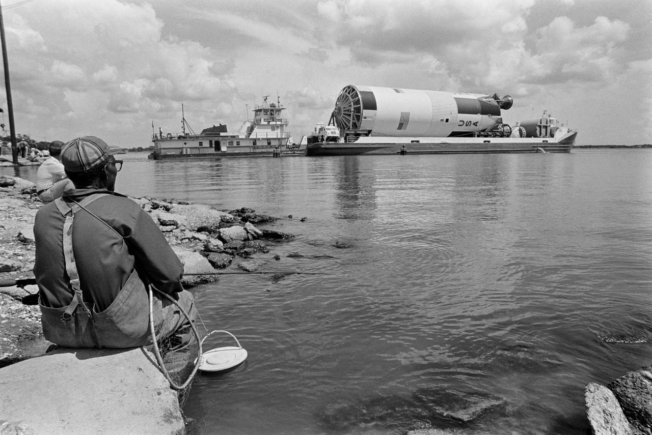 Views documenting the arrival of the Saturn V first stage at the Clear Lake dock near JSC after being transported via barge from Michoud Facility to be put on exhibit at JSC near Building 14.  Barge approach with fisherman and others onshore watching.           Houston, TX