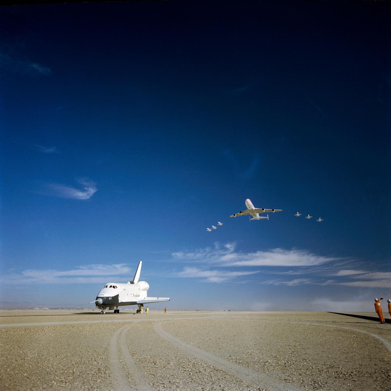 S77-28541 (23 Sept 1977) --- The NASA 747 carrier aircraft and six T-38 jets fly over the shuttle Orbiter 101 "Enterprise" soon after completion of a five-minute, 34-second unpowered mission during the third of a series of Shuttle Approach and Landing Tests (ALT) free-flights. Crew for the September 23, 1977, flight were astronauts Fred W. Haise Jr., commander, and C. Gordon Fullerton, pilot. Touchdown was 786 feet beyond aim point in the desert land of Edwards Air Force Base in Southern California.