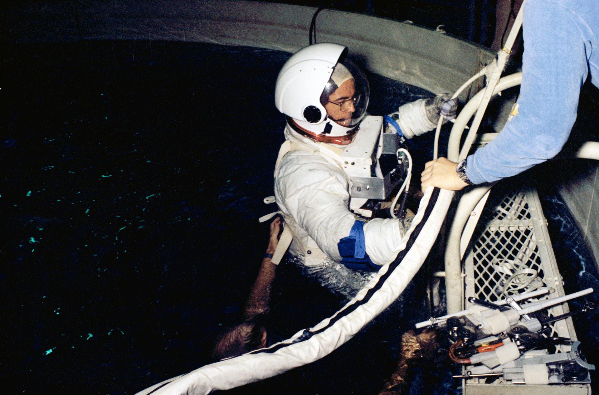 Astronaut Robert L. Crippen in a white EVA suit eases into a water immersion facility