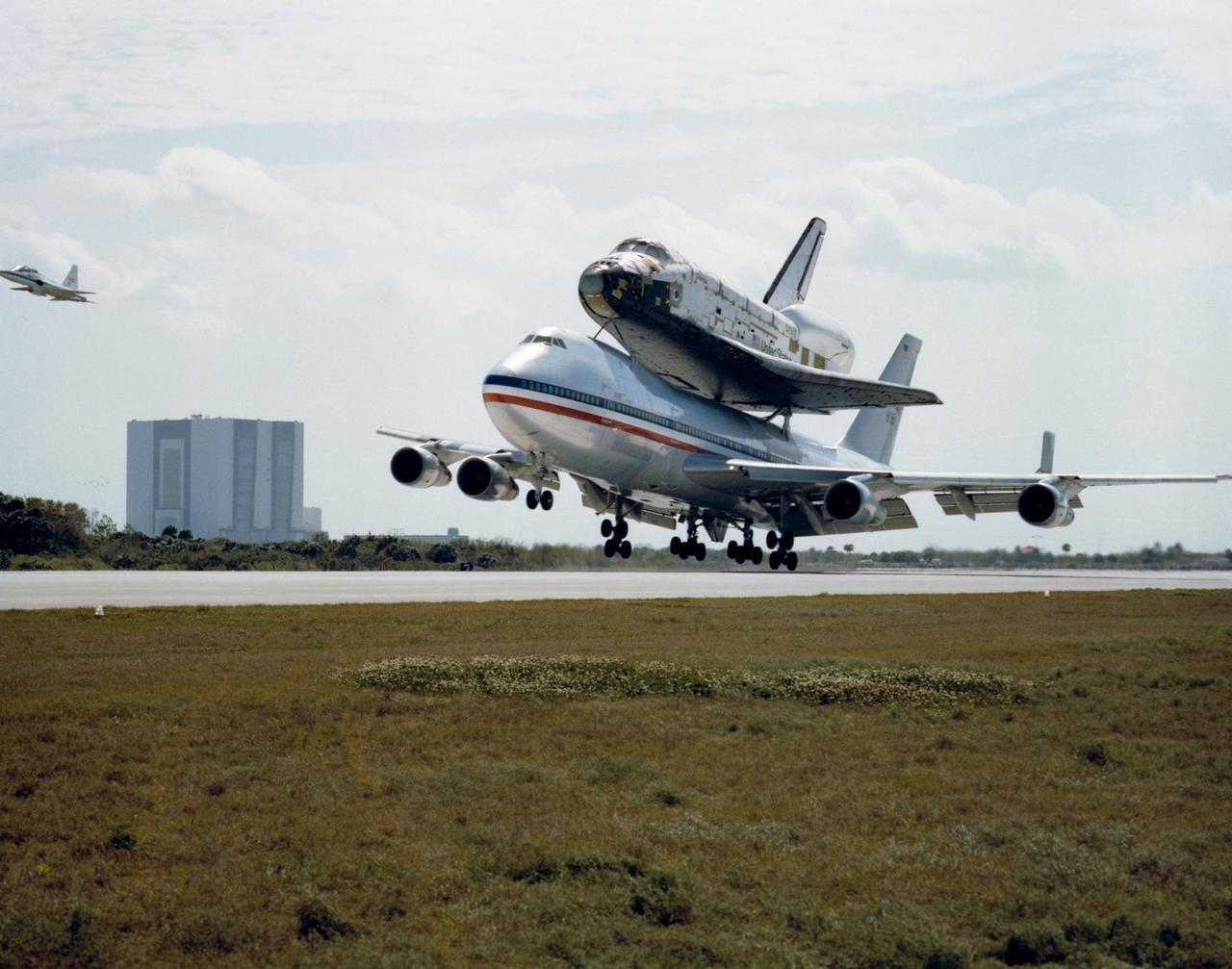 S79-30819 (24 March 1979) --- The space shuttle orbiter 102 Columbia riding ?piggyback? on NASA 905, a 747 carrier aircraft, is only seconds away from landing on Kennedy Space Center?s Shuttle landing facility, ending a 2,400-mile ferry flight from California. The T-38 chase plane at left is flown by Donald K. Slayton, manager for the orbital fight test (OFT) program. Columbia will be used for the OFT program, and it will be manned by astronauts John W. Young and Robert L. Crippen the first time it flies in space. The vehicle assembly building (VAB) is in right background. Photo credit: NASA