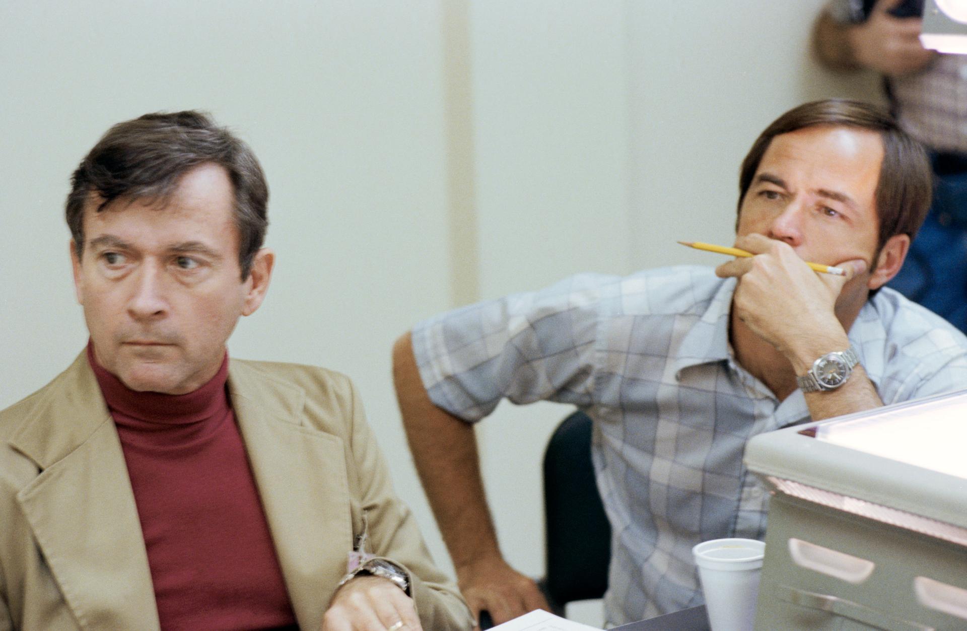 STS-1 astronauts John W. Young and Robert L. Crippen sit at a table staring intently
