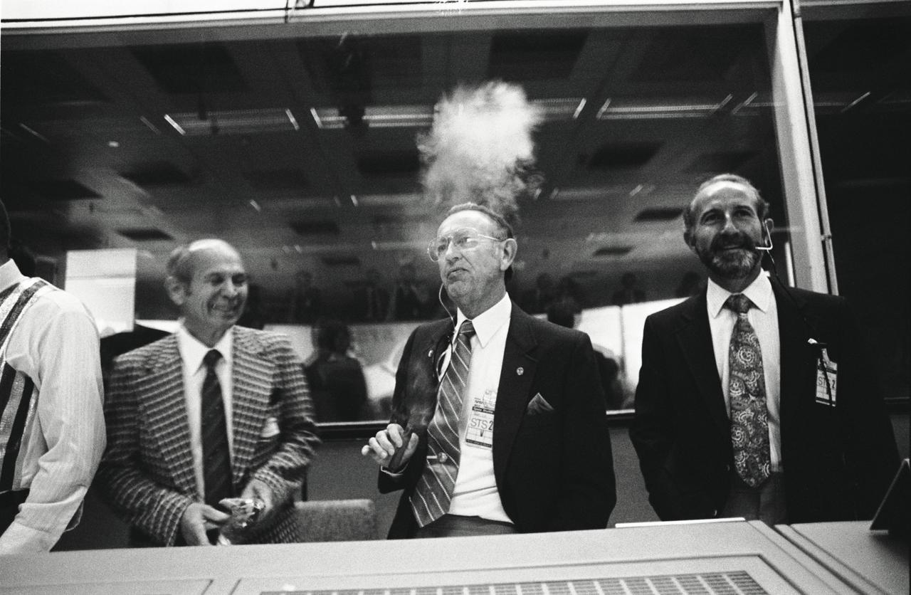 S81-39508 (14 Nov. 1981) --- The successful STS-2 landing at Edwards Air Force Base in California was cause for celebration in the Johnson Space Center?s Mission Control Center shortly before 3:30 p.m. (CST) on Nov. 14, 1981. JSC Director Christopher C. Kraft Jr. (center), enjoys a traditional ?touchdown? cigar. He is flanked by retiring lead engineer Maxime Faget (left) and Thomas L. Moser of the structures and mechanics division, who join the celebration. The second flight of the space shuttle Columbia lasted two days, six hours, 13 minutes and a few seconds. Photo credit: NASA