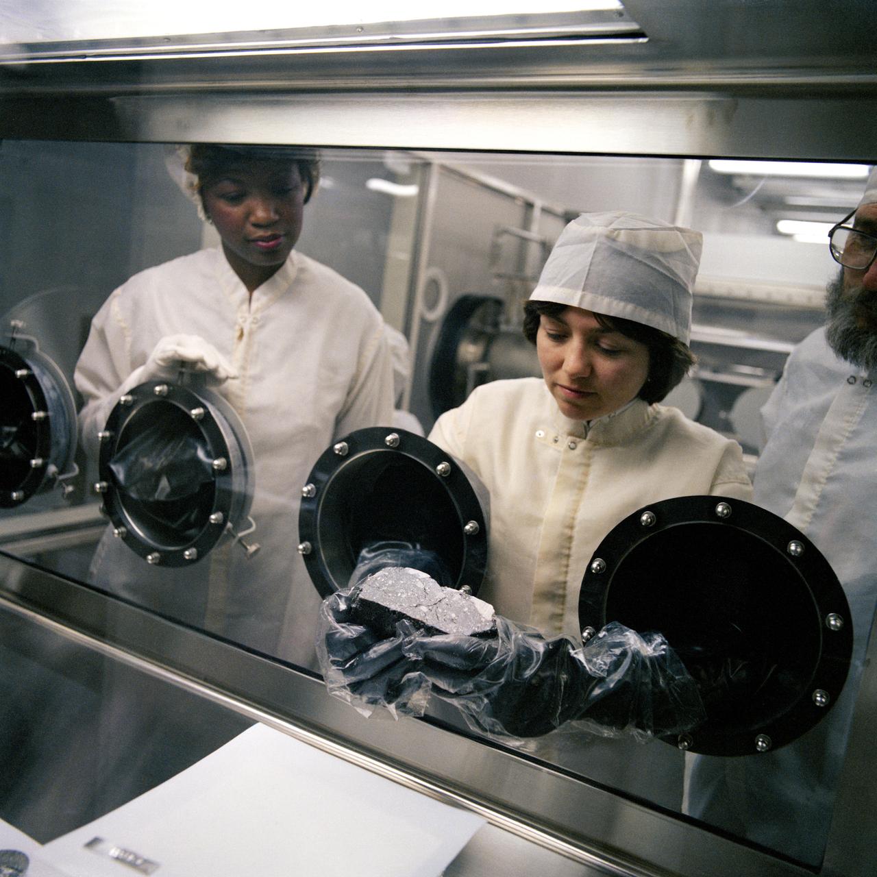 S82-26777 --- Technicians examine lunar samples in a glovebox at NASA's Johnson Space Center in Houston.