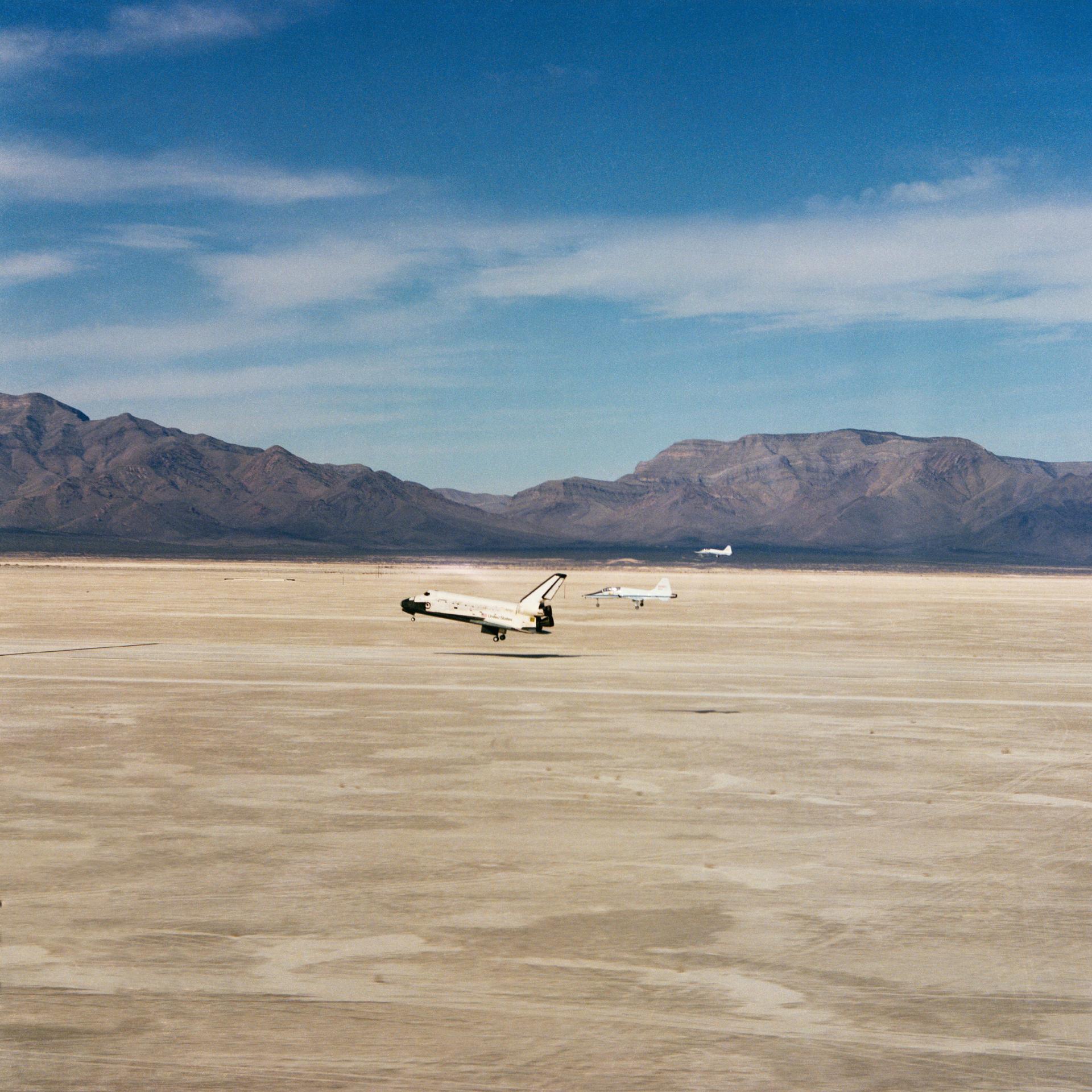 Space Shuttle Columbia is seen landing in the New Mexico desert with mountains in the background.