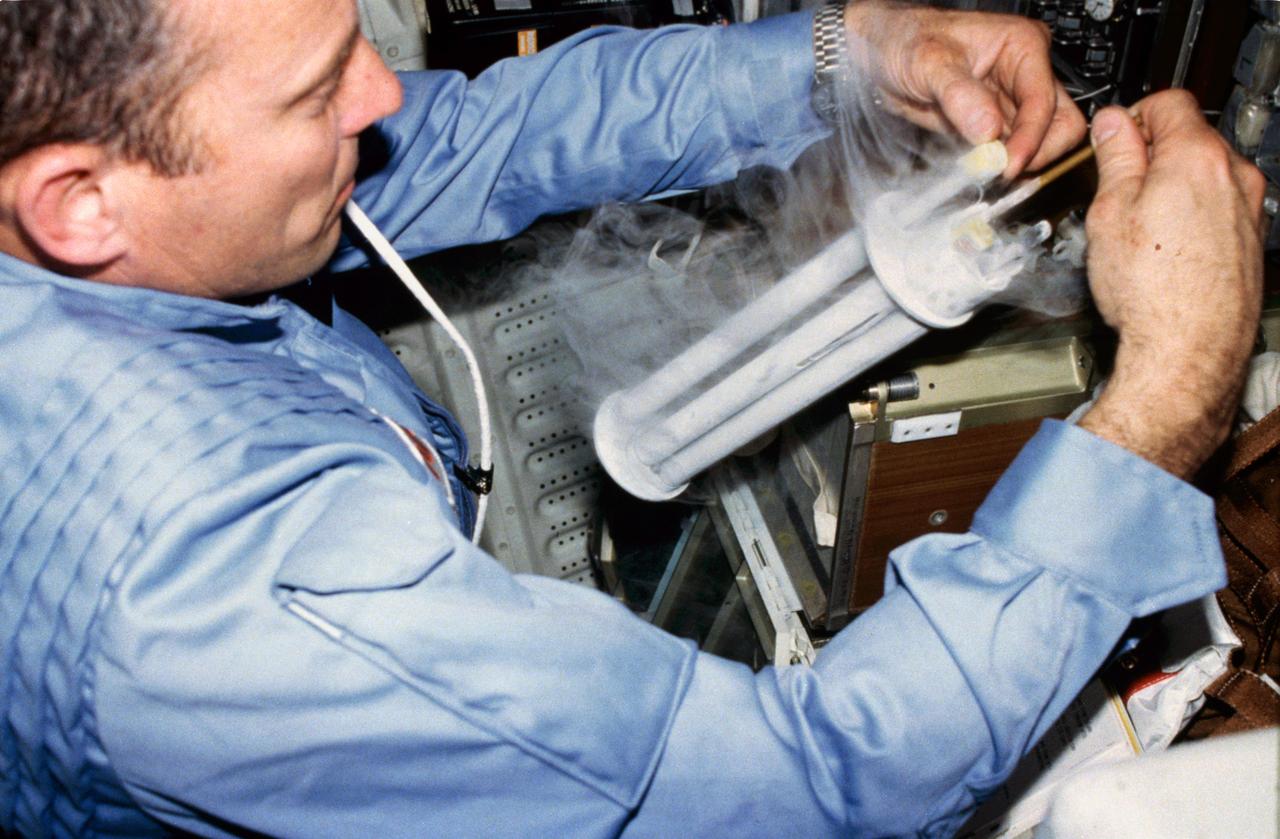 Commander Jack Lousma works with Electrophoresis Equipment Verification Test (EEVT) electrophoresis unit, cryogenic freezer and tube, and stowage locker equipment located on crew compartment middeck aft bulkhead.