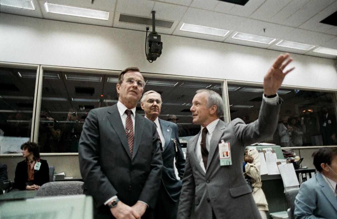 S83-30193 (8 April 1983) --- Vice President George Bush, left, is briefed by JSC Director Gerald D. Griffin, right, during a visit to the mission operations control room (MOCR) in the Johnson Space Center?s mission control center. James Beggs, NASA administrator, center, accompanied the Vice President on his visit.  Flight Director Gary E. Coen is partial visible at right edge of frame, The photograph was taken by Otis Imboden.