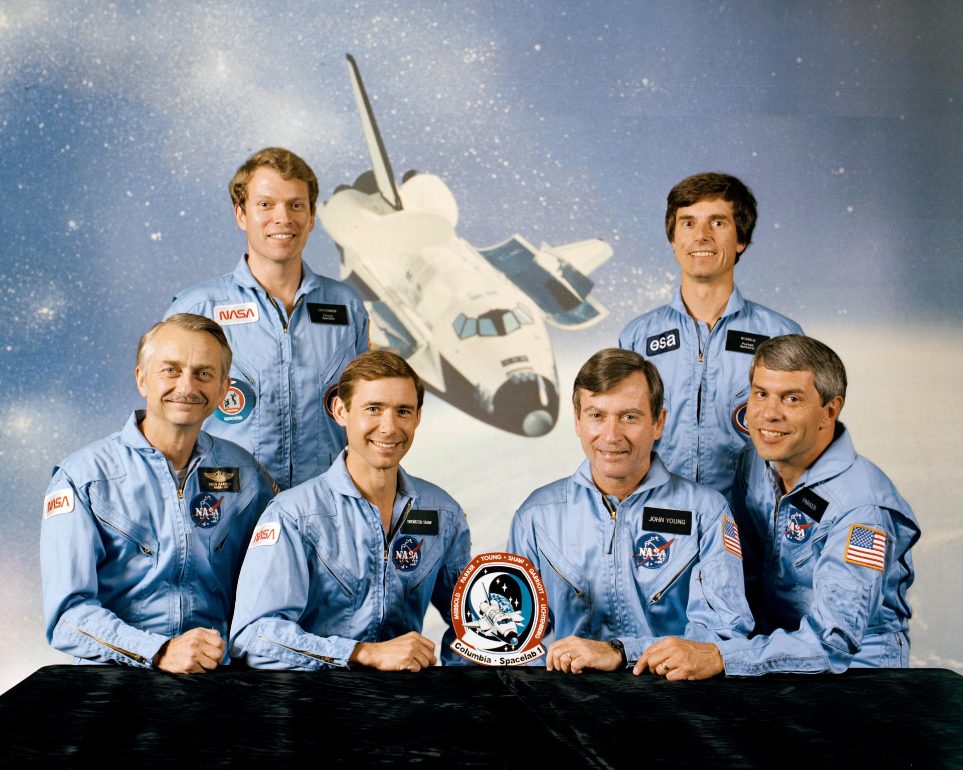 Six men pose in front of an orbital scene featuring the Columbia