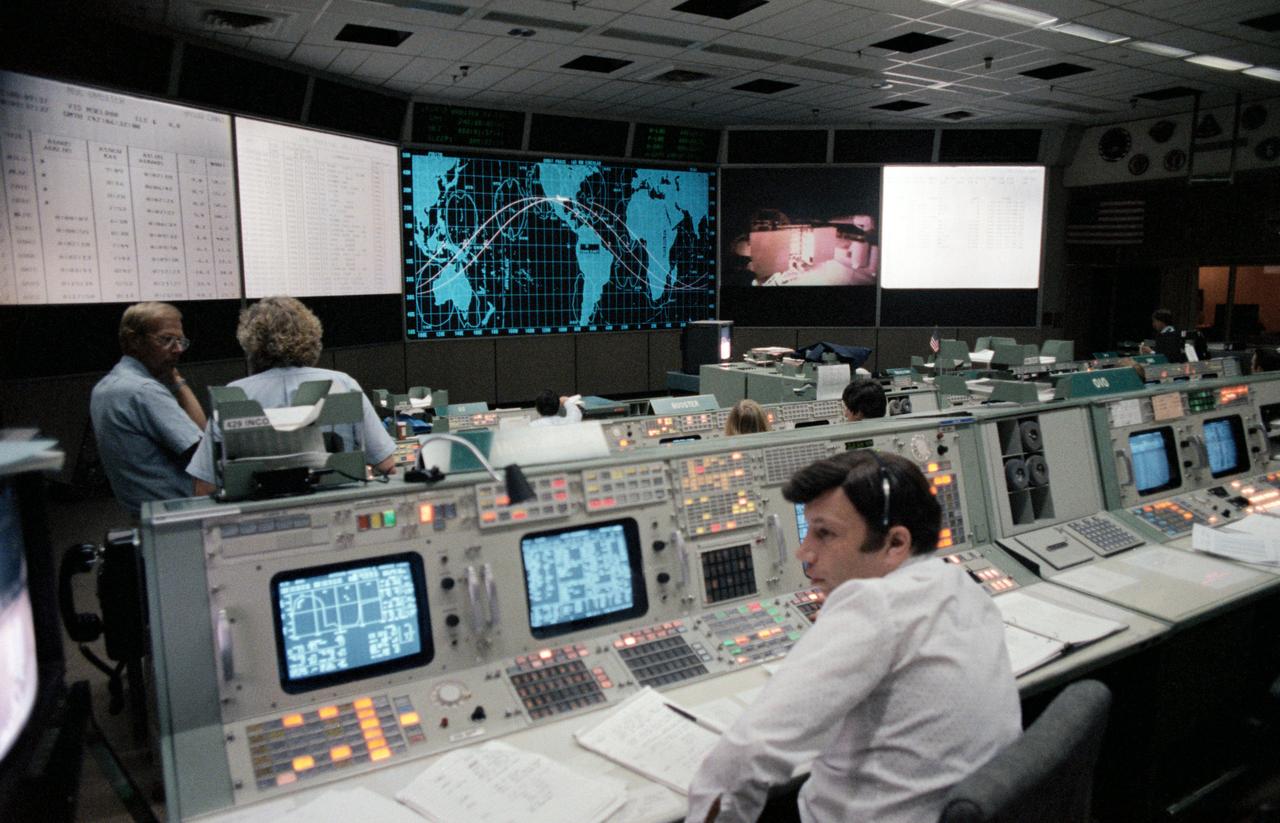 Serving as spacecraft communicators (CAPCOM) are Astronauts Guy S. Gardner (left), William F. Fisher (center), Bryan D. O'Connor (seated facing console), and Jeffrey A. Hoffman. Cheevon B. Lau is seated at the flight activities officer (FAO) console to the right of the CAPCOM console. The scene on the large screen in the mission operations control room (MOCR) is a replay of the launch of the Challenger (39264); Flight Director Jay H. Greene, left, watches a replay of the STS-8 launch on the large screen in the MOCR. He is joined by O'Connor, Jeffrey A. Hoffman, Gardner and Fisher. Lau works at the FAO console near the CAPCOM console (39265); Harold Black, integrated communications officer (INCO) for STS-8 mans the INCO console during the first TV downlink from the Challengers flight. The payload bay can be seen on the screen in the front of the MOCR (39266).