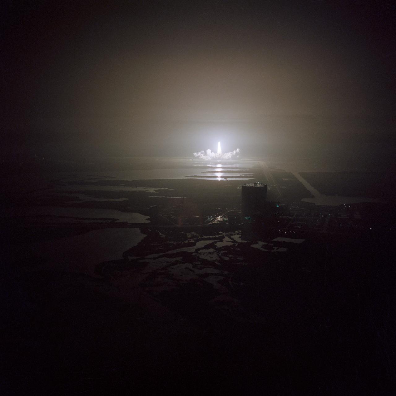 S83-39567 (30 Aug. 1983) --- The nighttime liftoff of the space shuttle Challenger casts a brilliant glow across the marshy Kennedy Space Center (KSC) landscape. This aerial view from west of the vehicle assembly building (VAB) shows the Challenger climbing toward space just after its 2:32 a.m. (EDT) launch to begin the STS-8 mission. Photo credit: NASA