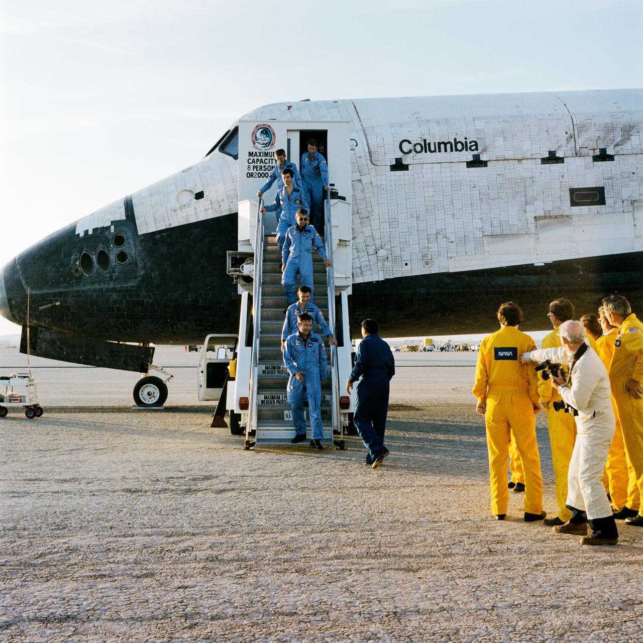 S83-45648 (8 Dec 1983) --- After more than 10 days in Earth orbit, the crewmembers for STS-9 egress the Space Shuttle Columbia following its successful landing at Edwards Air Force Base in southern California. Descending the stairs are (from bottom) Astronaut John W. Young, Brewster H. Shaw Jr. and Robert A. R. Parker; West German physicist Dr. Ulf Merbold; Astronaut Owen K. Garriott, and Dr. Byron K. Lichtenberg, a biomedical engineer from the Massachusetts Institute of Technology. Young was STS-9 crew commander; Shaw, pilot Drs. Parker and Garriott were mission specialists; and Drs. Merbold and Lichtenberg, payload specialists. Dr. Merbold was the European Space Agency?s first scientist to fly aboard a NASA spacecraft and Dr. Lichtenberg was America?s first non-astronaut to join a NASA crew in space. On hand to greet the crewmembers is George W. S. Abbey, director of flight crew operations.