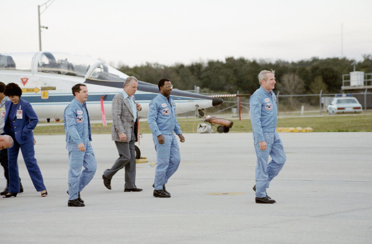 S84-26935 (31 Jan 1984) --- Three members of the STS 41-B astronaut crew arrive in Florida following a brief T-38 flight from Houston. Leading the crew from the flight line is Astronaut Vance D. Brand (right), crew commander. Following behind (in blue flight suits) are Astronauts Ronald E. McNair (center) and Robert L. Stewart (both mission specialists. They were met by Terry White (pictured), JSC public information industrial relations manager. Not pictured are Astronauts Robert L. Gibson, pilot; and Bruce McCandless II, mission specialist. Launch is scheduled for February 3, 1983.