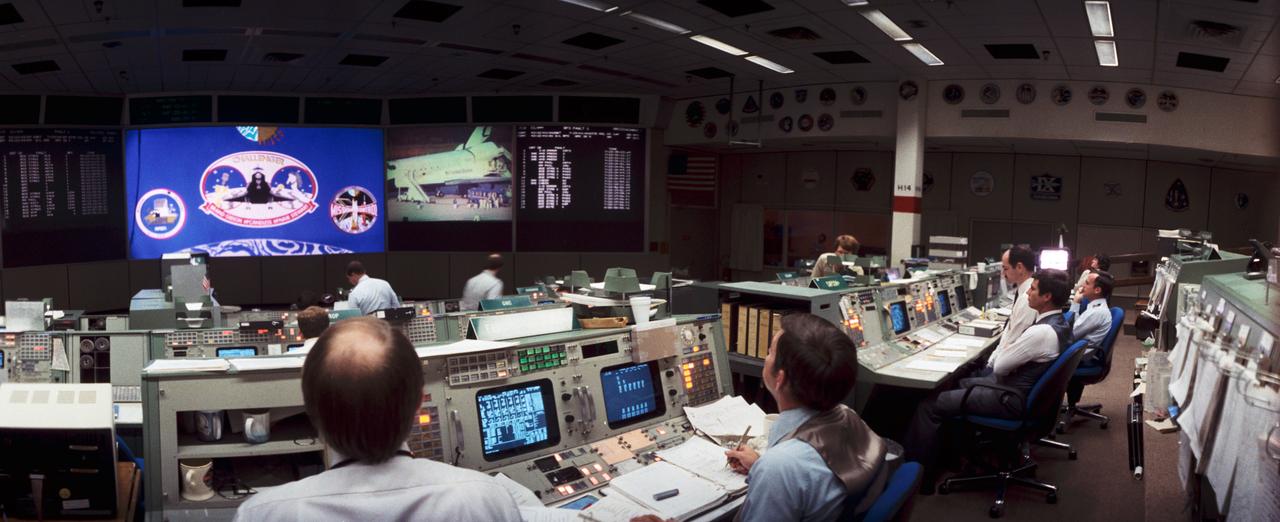 S84-26977 (11 Feb 1984) --- Flight Director Randy Stone, left, and Gary Coen, center foreground, watch a monitor in the front of the mission operations control room (MOCR) to stay attuned to post-landing activity at the KSC facility in Florida.  MOCR is the Johnson Space Center?s mission control center.  Astronauts John E. Blaha and Guy S. Gardner man the spacecraft communicator (CAPCOM) console in the background.  The Space Shuttle Challenger, having just completed its fourth mission in earth orbit and weighing some 201,600 pounds, can be seen on the monitor.