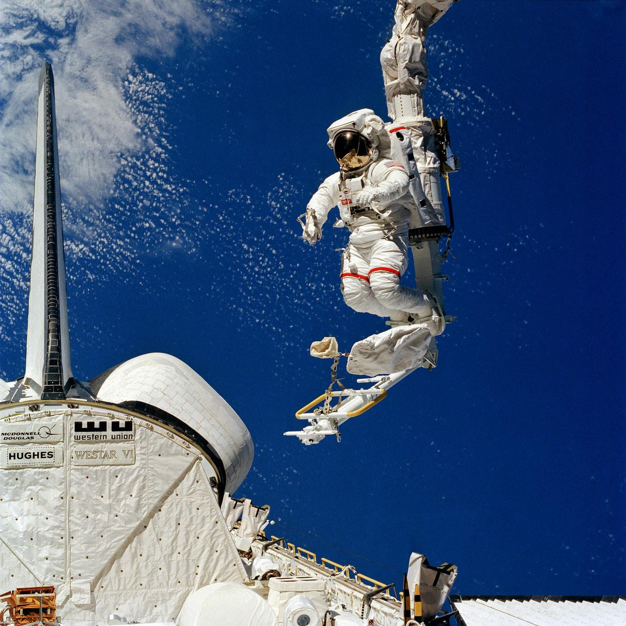 S84-27040 (7 Feb 1984) --- Some have called it NASA's first "cherry picker" in space. Others simply call it the mobile foot restraint (MFR) connected to the remote manipulator system (RMS).  Astronaut Bruce McCandless II, pictured leaning out into space as his feet are anchored in the MFR, and moved around by the RMS, calls it a look of things to come. The aft portion of the Challenger, to which the RMS is connected, is seen in lower left corner. This photograph is one of a sequence showing McCandless in the device. On this same EVA, McCandless also initiated use of the manned maneuvering unit (MMU), not pictured here, a nitrogen-propelled back pack apparatus allowing for free movement in space.